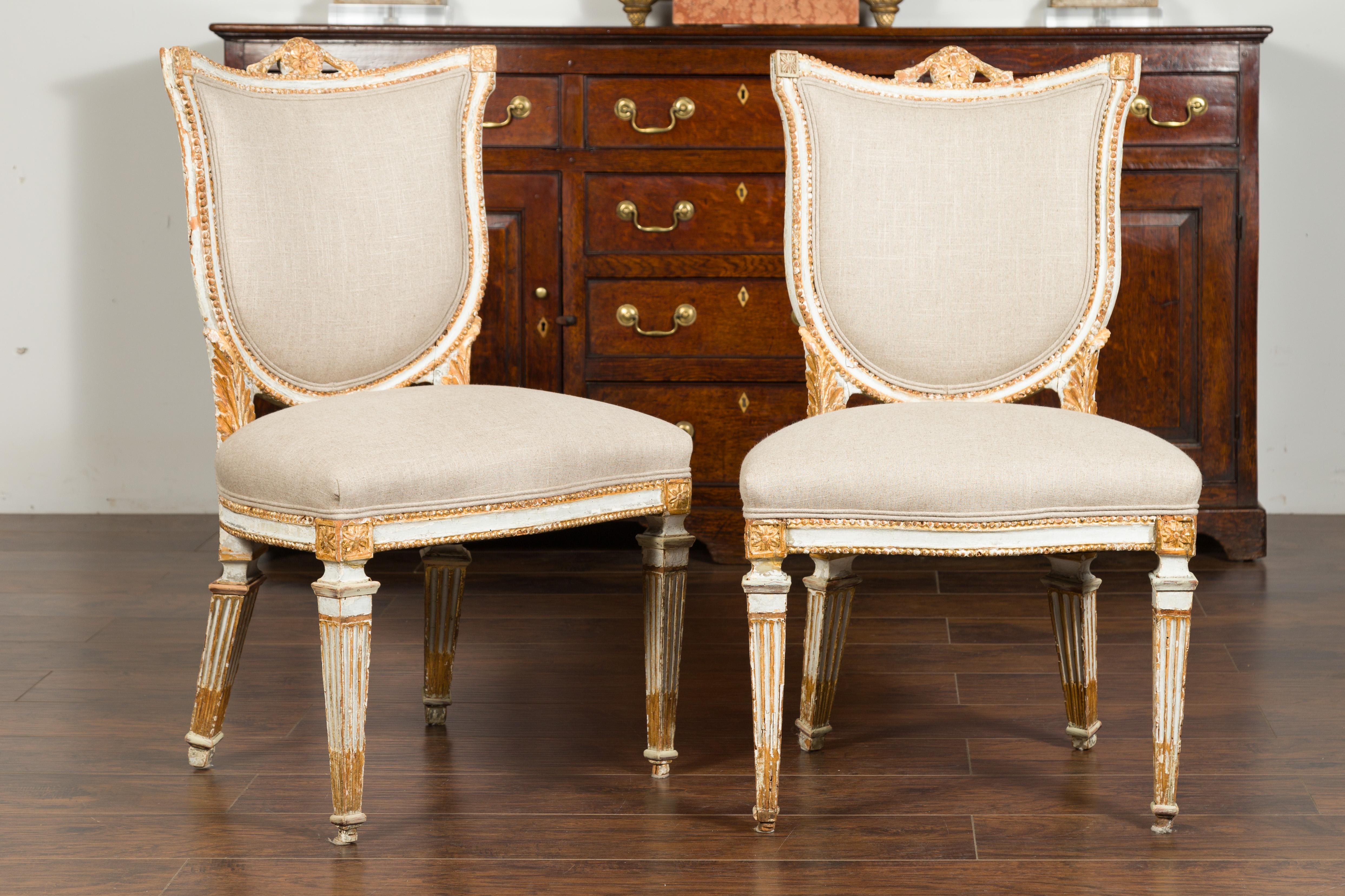 A pair of Italian 1790s neoclassical painted and carved side chairs with shield backs and traces of gilt. This pair of Italian neoclassical side chairs from the late 18th century is quite a show stopper! Each chair has a shield-shaped back, adorned