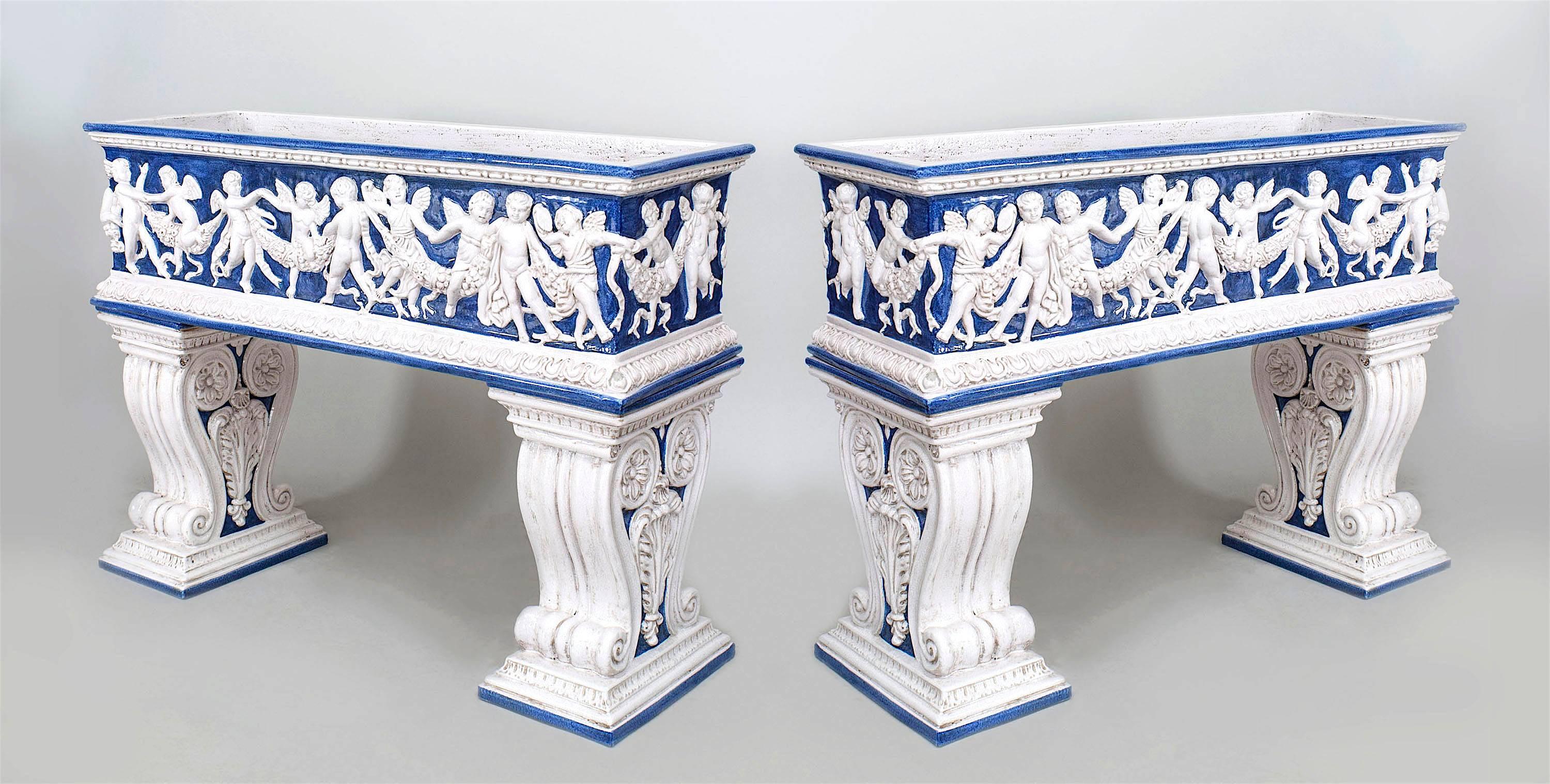 Pair of Italian Neo-classic (19/20th Cent) blue and white glazed terra-cotta rectangular planters/ferneries raised on a Pair of scroll pedestals with cupids and garlands in relief.
