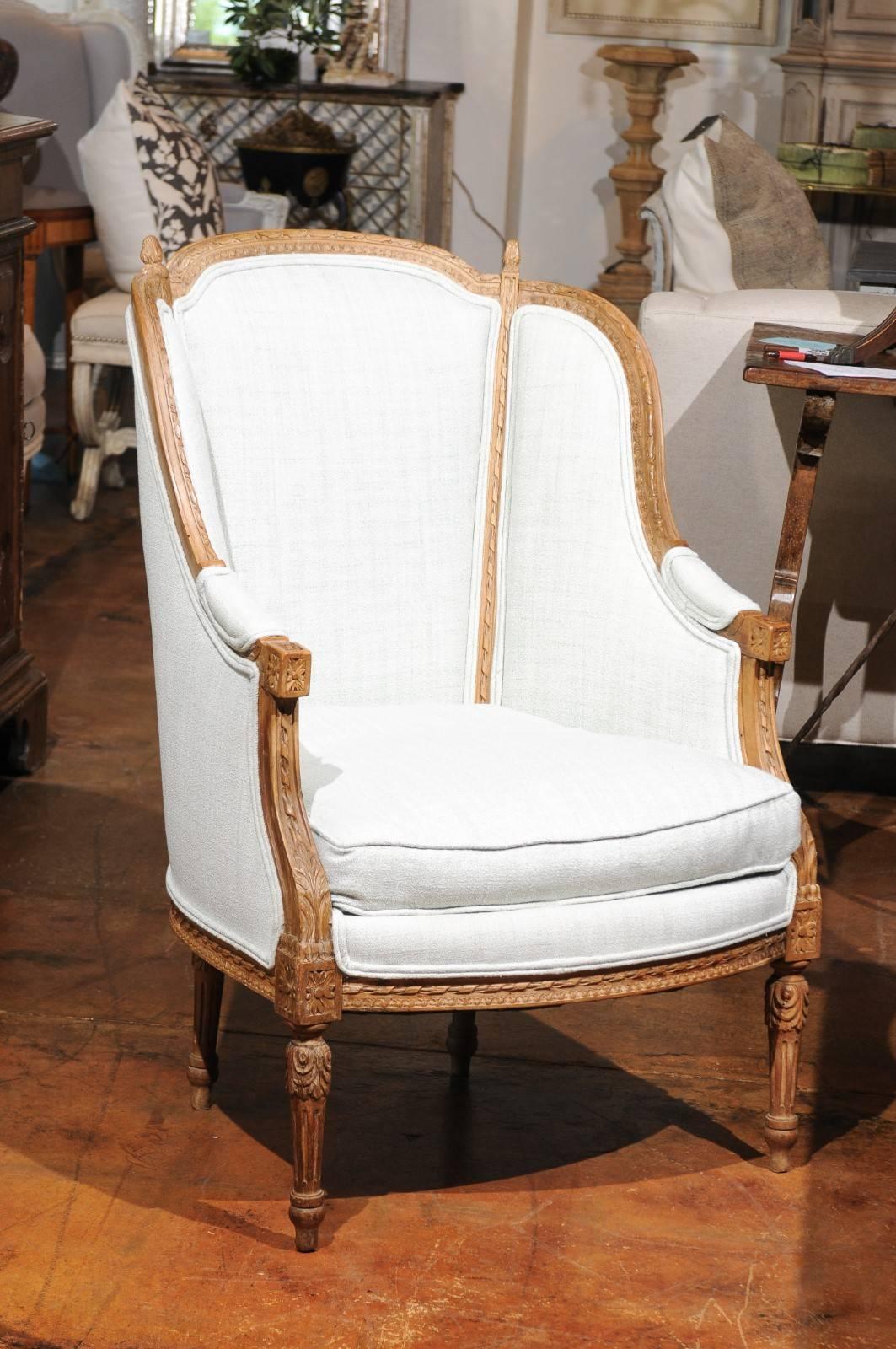 A pair of Italian Neoclassical style richly carved wingback bergères chairs from the 19th century, with new upholstery. Each of this pair of Italian bergères armchairs features an upholstered winged back, adorned with carved moldings on the upper