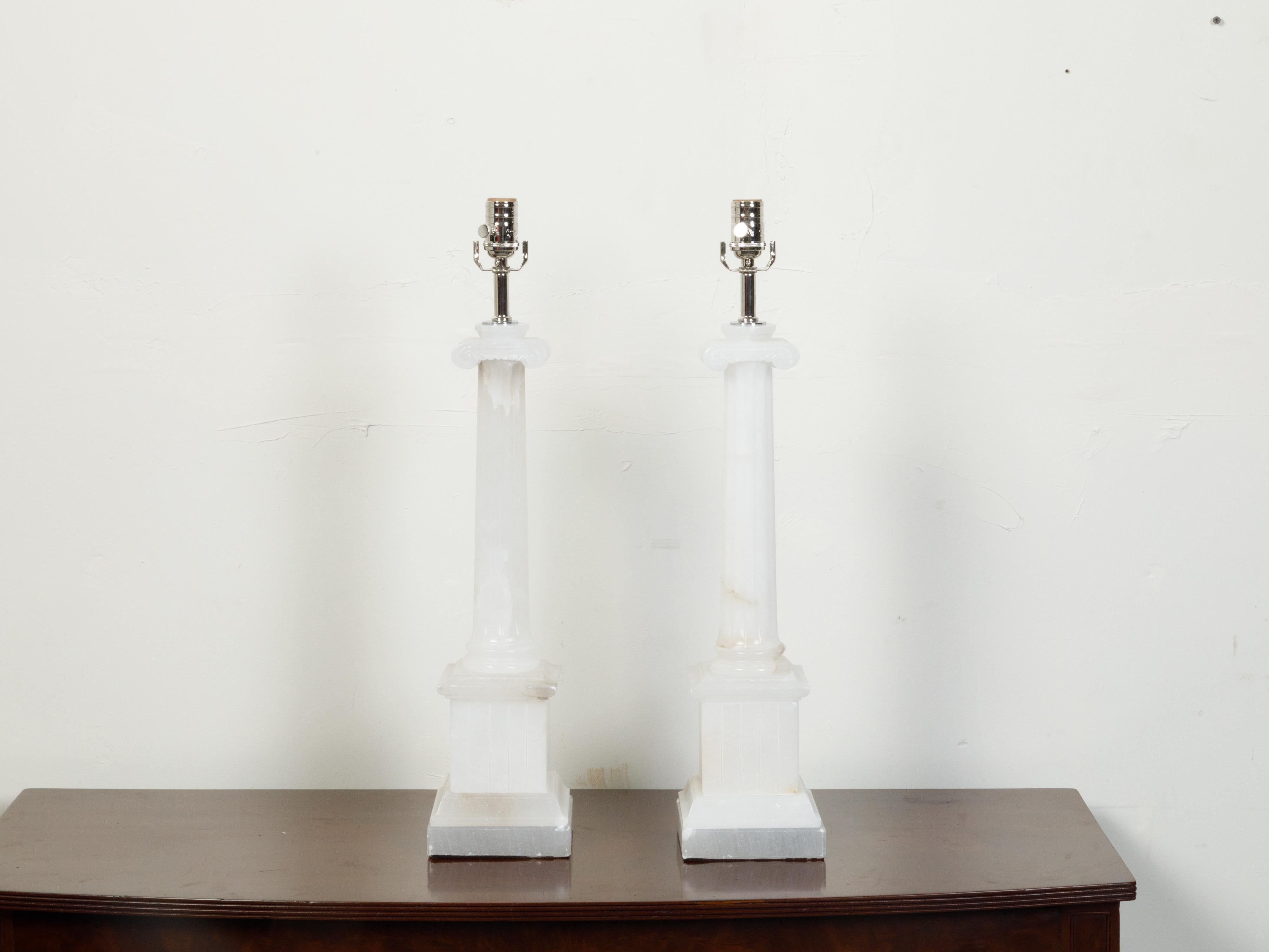 A pair of Italian Neoclassical style vintage alabaster table lamps from the mid 20th century, with Ionic columns on tall pedestals. Created in Italy during the midcentury period, each of this pair of alabaster lamps captures our attention with its