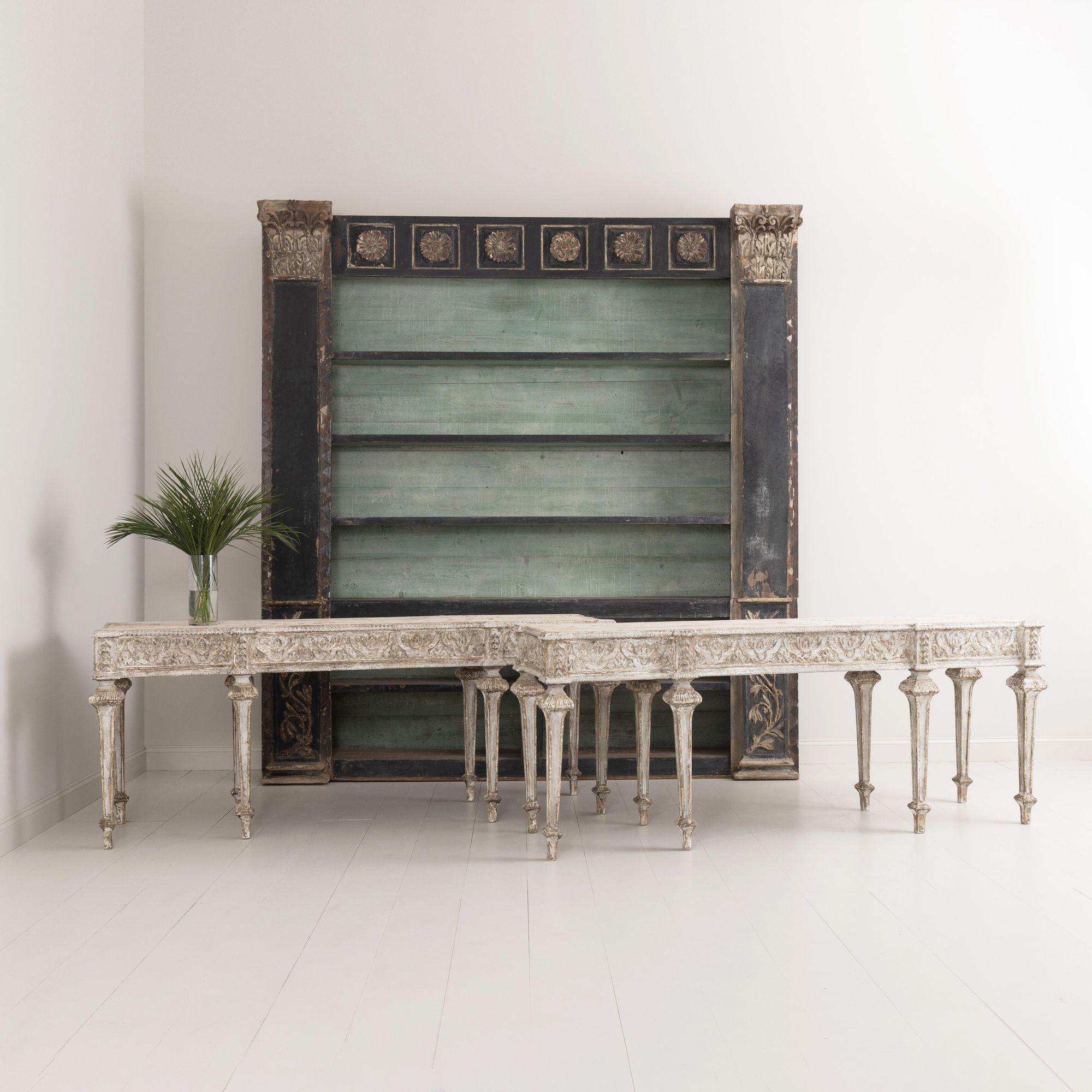 A pair of large Italian painted console tables in the Neoclassical style. Beautifully carved aprons with bell flowers on the corner posts above square caps, ending in tapered legs. 


We offer expedited, fully-insured, custom packaged / crated,