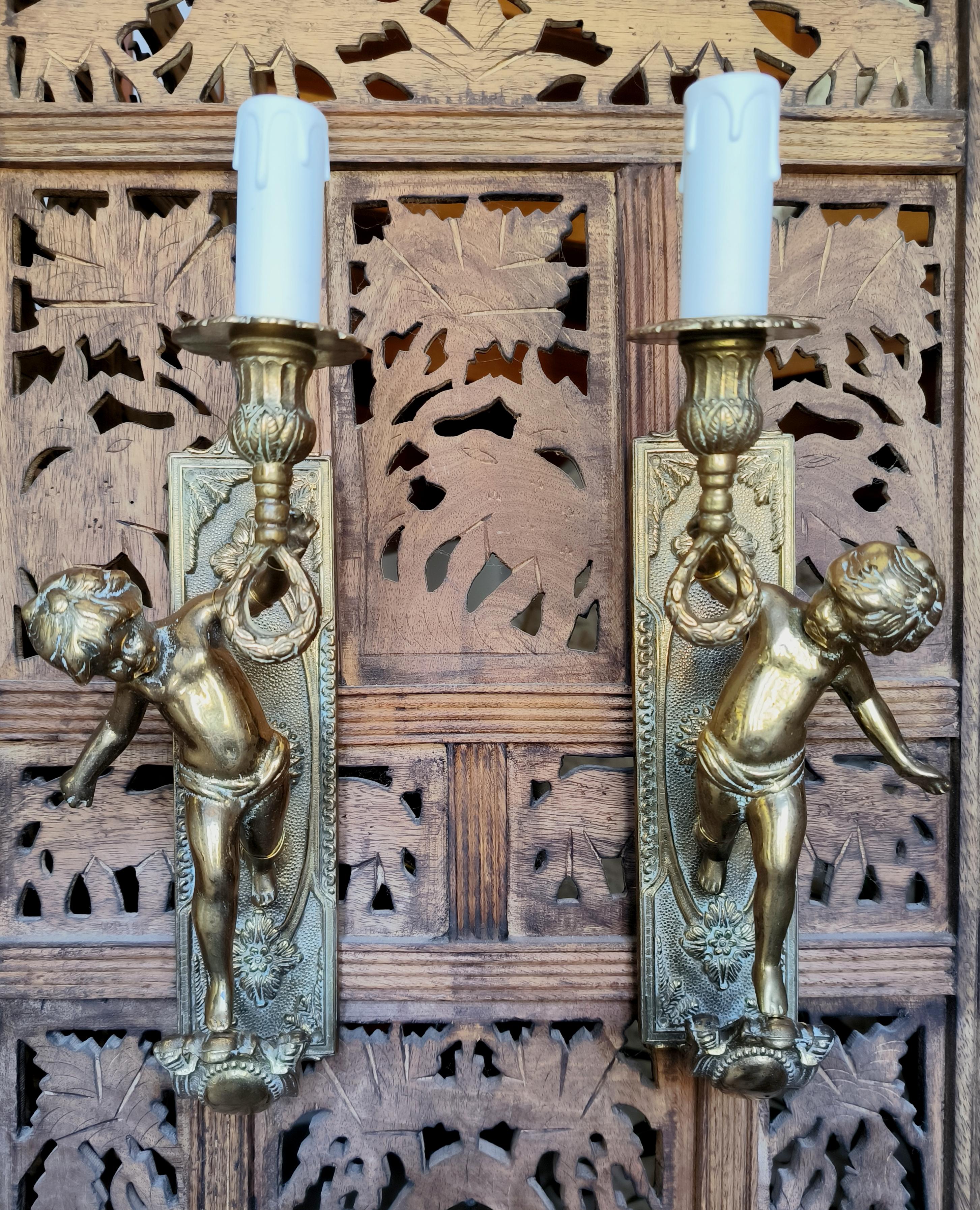 Beautiful pair of handmade Italian, bronze, opposing cherub / putti wall sconces, circa mid 20th century. The sconces show wonderful weight and quality and have gorgeous detail. Depicting traditional neoclassical themes, the sconces are in generally