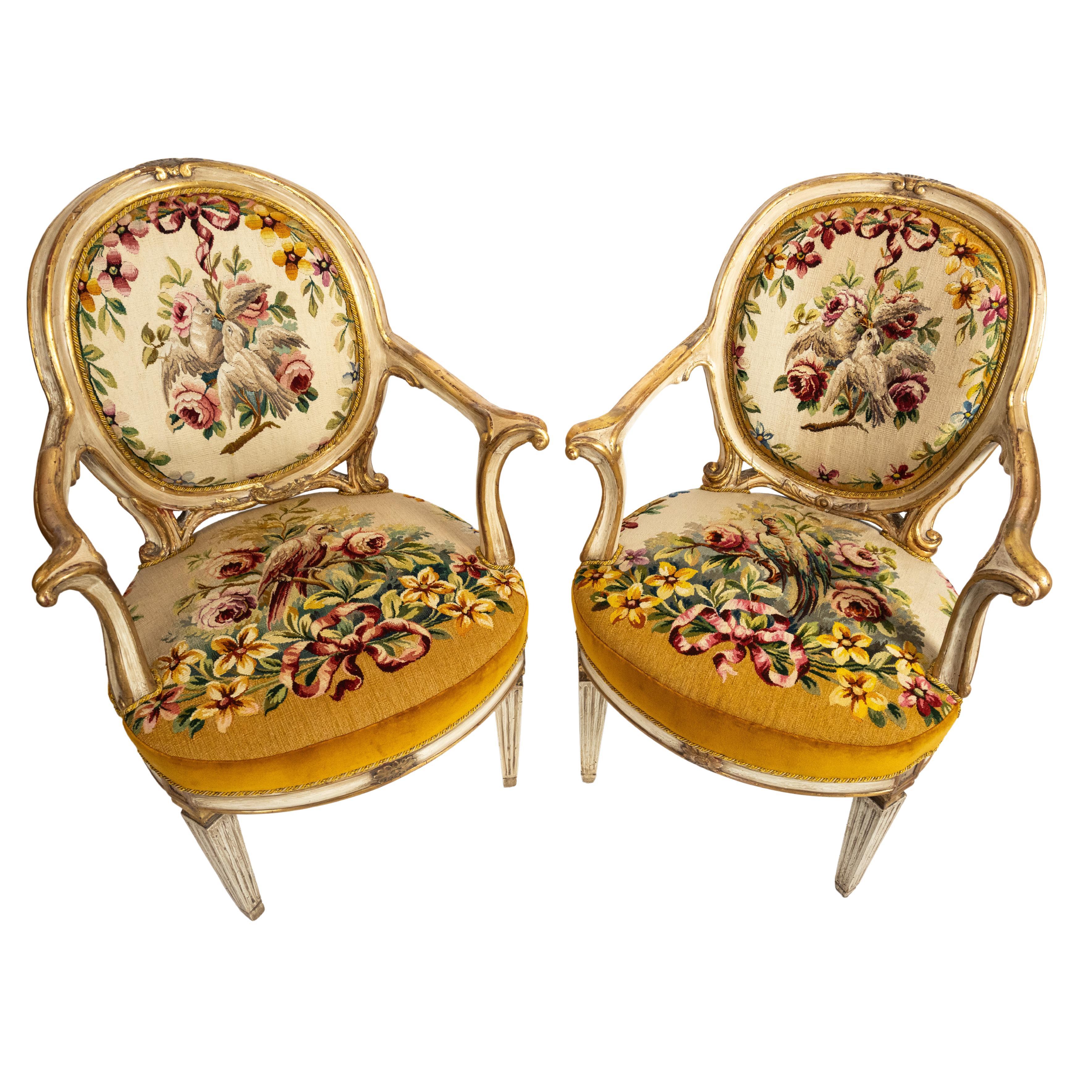 A pair of Italian Neoclassical open arm chairs with carved white painted frames having gilt details. The oval chairbacks and seats are upholstered with French Aubusson tapestry, having polychrome floral and bird motifs accented by bows. The frames