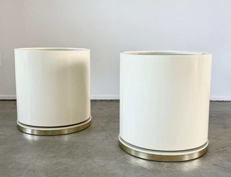 Sexy pair of 1970's Italian bedside tables in lacquered cream wood and brass top. End tables have door that swings open to reveal shelving and float on a brass plinth base.