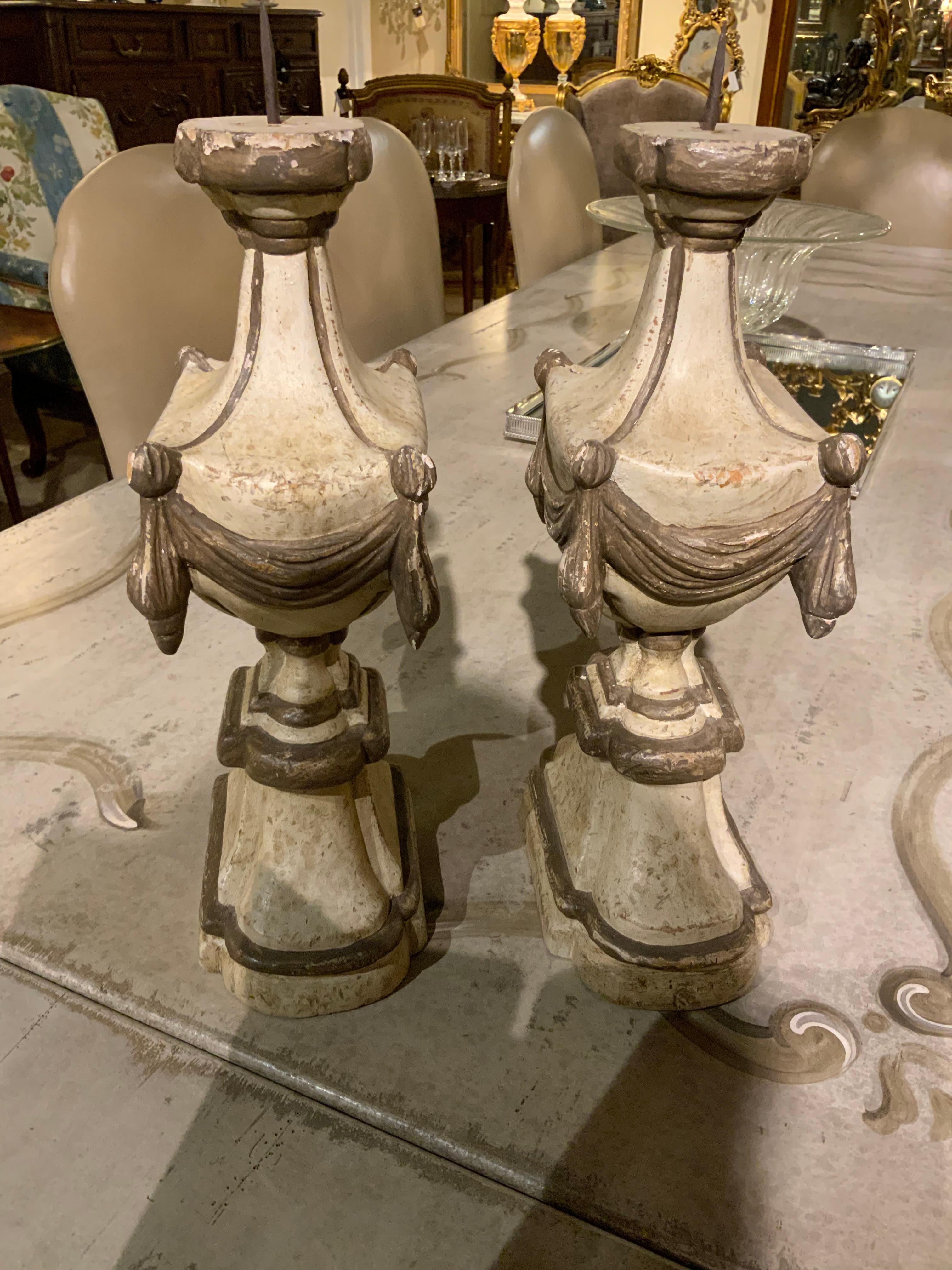 Pair of hand painted and carved wooden candle holders having
a metal spike to hold candles. They are painted in a cream/ grey tone.
That is very pleasing and have a carved swag painted in a deeper tone.
A rim at the top is also painted in a