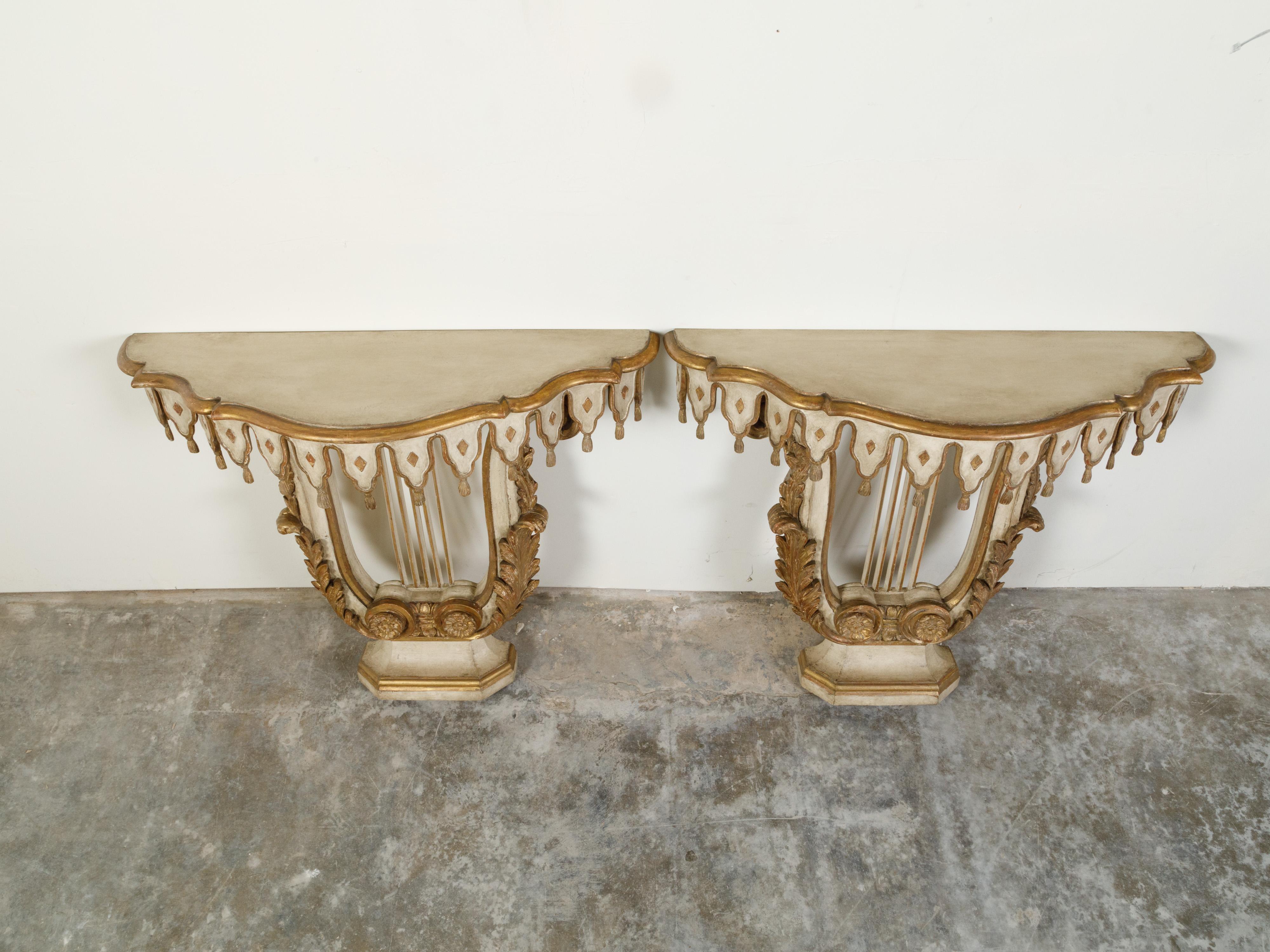 A pair of Italian painted and gilded demilune console tables from the early 20th century, with tassel motifs and lyre-shaped bases. Created in Italy during the first quarter of the 20th century, these demilunes attract our attention with their