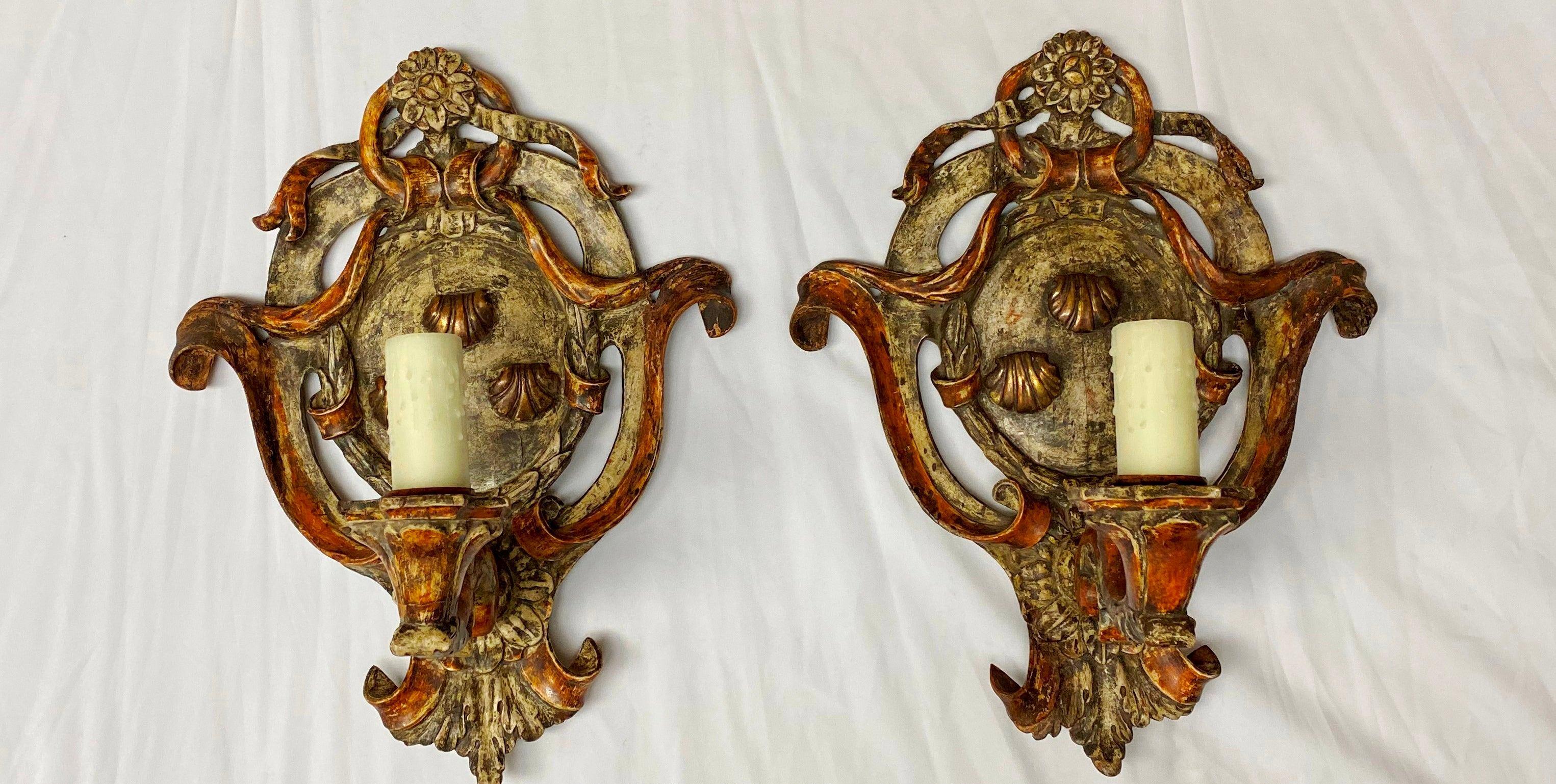 Pair of Italian Baroque style painted carved wood sconces, 19th century. 
Each surmounted with a rosette above a ribboned hand painted and parcel gilt cartouche, issuing a single hand carved foliate inspired candle arm terminating in a bees wax