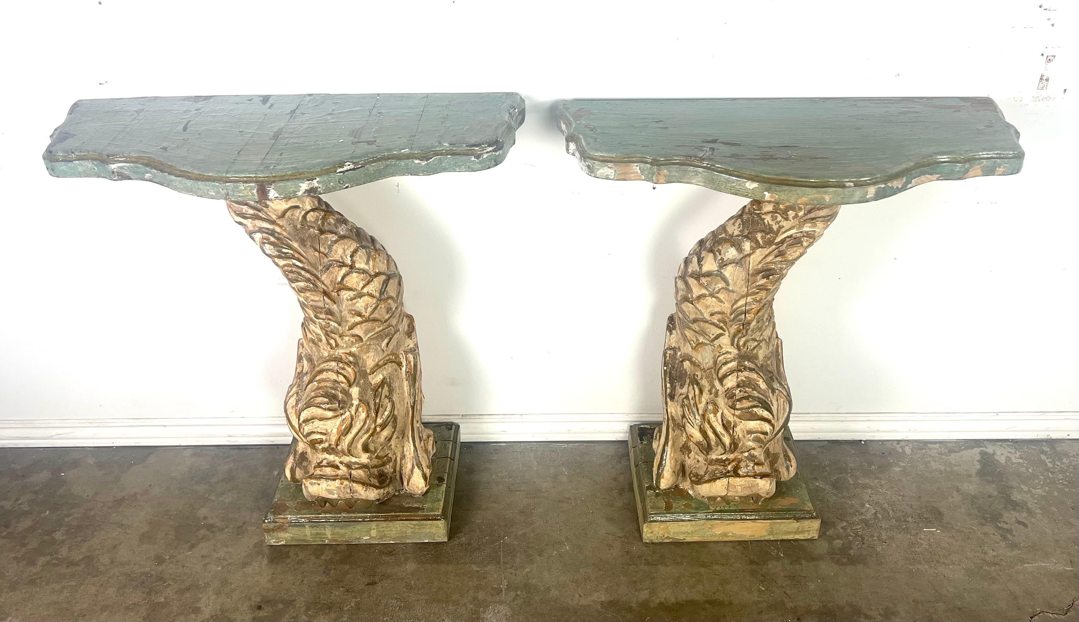 These consoles feature an intriguing and distinctive design, each supported by a sculpted base resembling a large, stylized fish or mythical sea creature, complete with scales and swirling patterns.

The bases are distressed, which adds to their