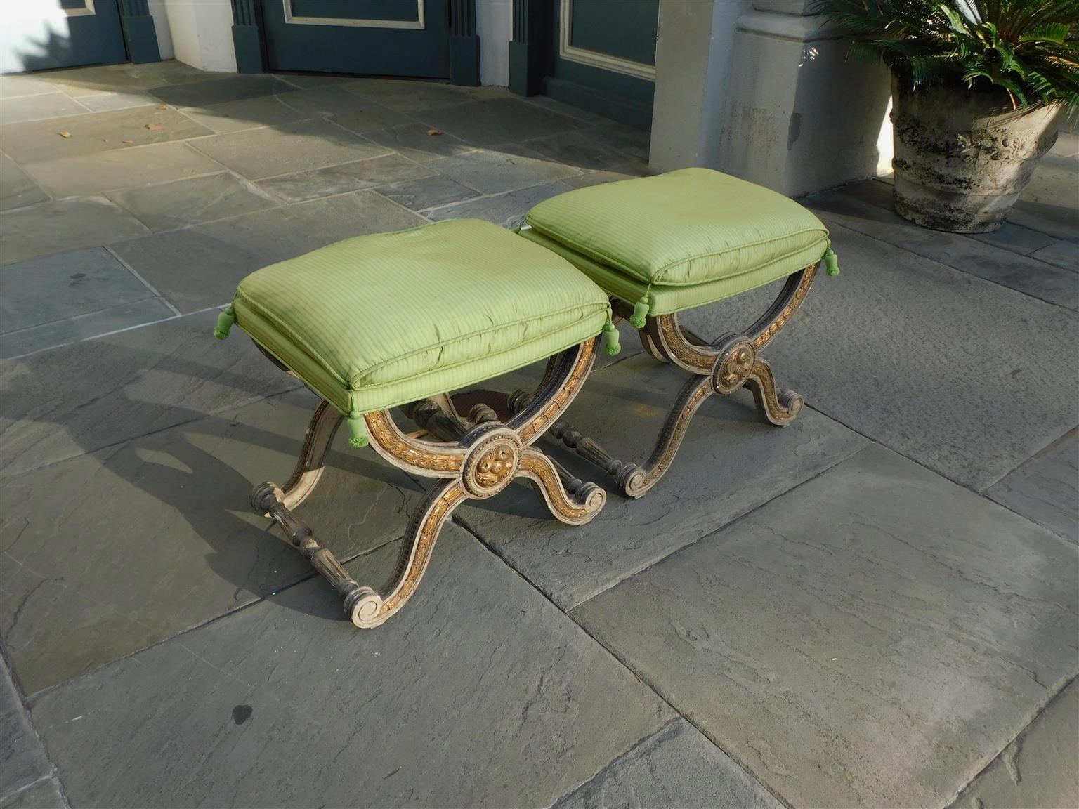 Pair of Italian painted and gilt wood foliate upholstered Curule stools with flanking central foliage medallions, and resting on scrolled feet with the original connecting cross stretchers, late 18th century.