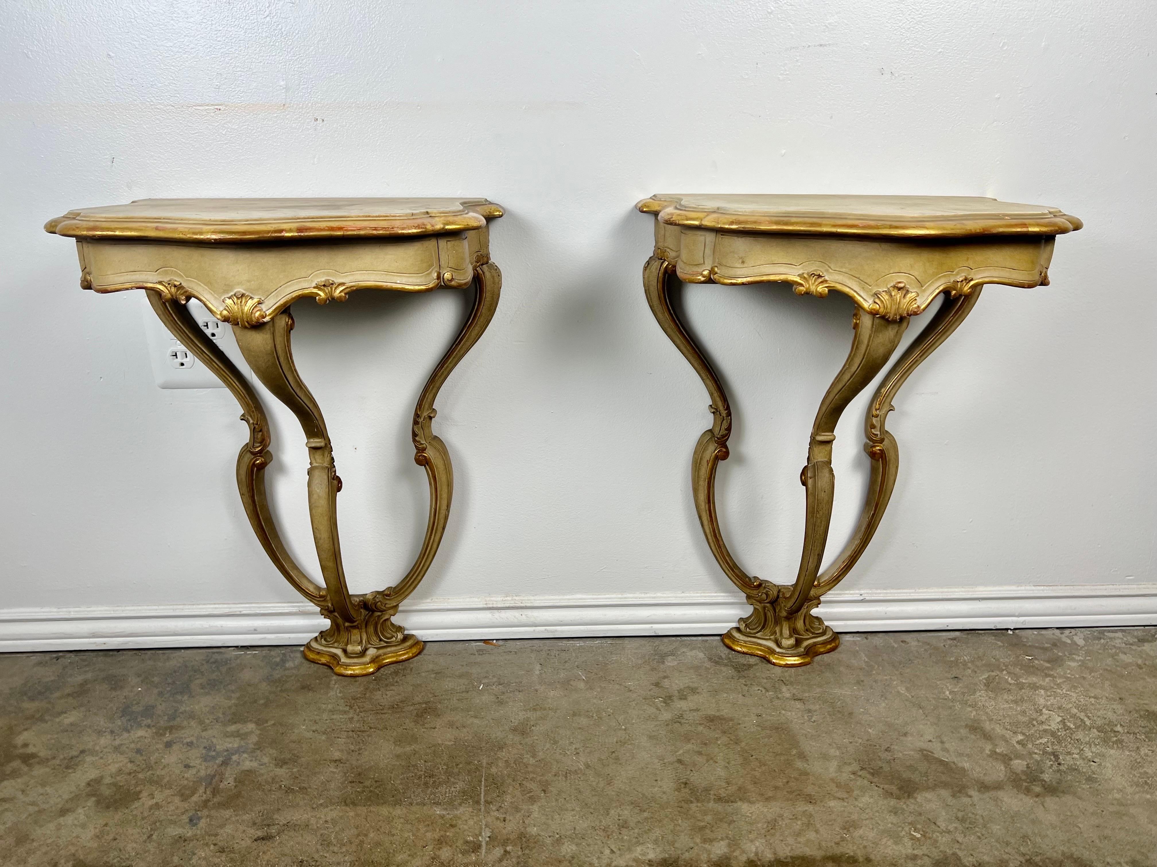 Pair of Italian painted & parcel gilt carved console with a serpentine shaped worn top.  The consoles have a nice shape with a tripod base that meets at the base of the table.  Gold leaf carved acanthus leaves throughout.  The consoles have drawers