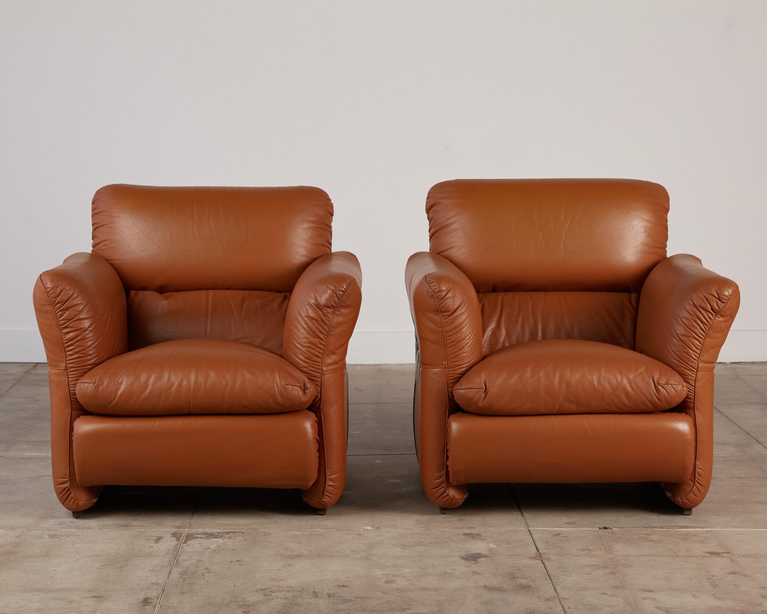 A pair of Italian leather armchairs in the style of De Sede. The chairs are made of tan colored leather with a linear wooden base. Upholstered in a beautiful soft leather, the headrest can be adjusted to lean back and the arms to fold out giving you