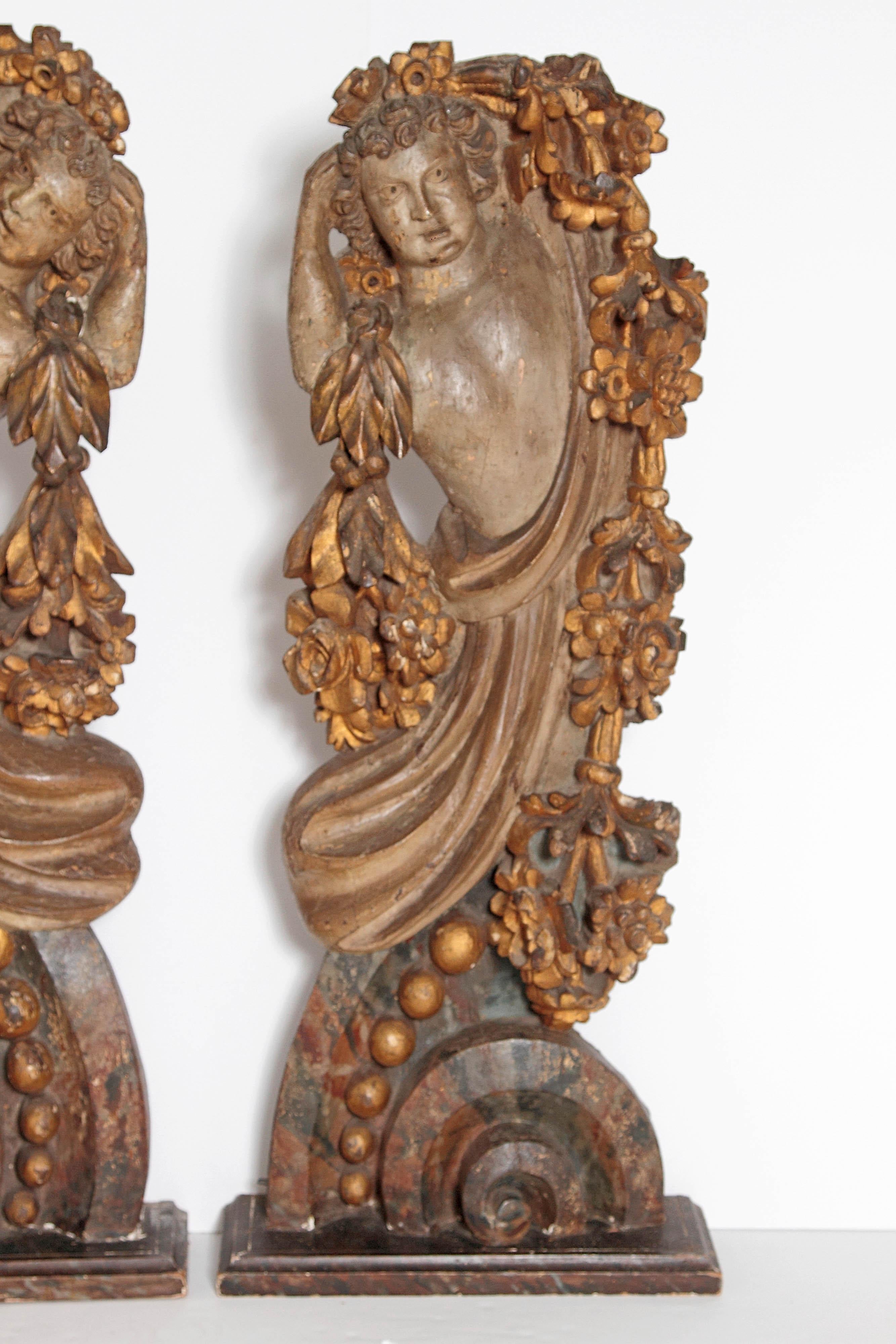 A pair of large freestanding Italian carved and polychromed figures or male torsos or upper bodies draped in garlands of leaves and flowers (architectural fragments, supports, or appliques) late 19th century, Italy.