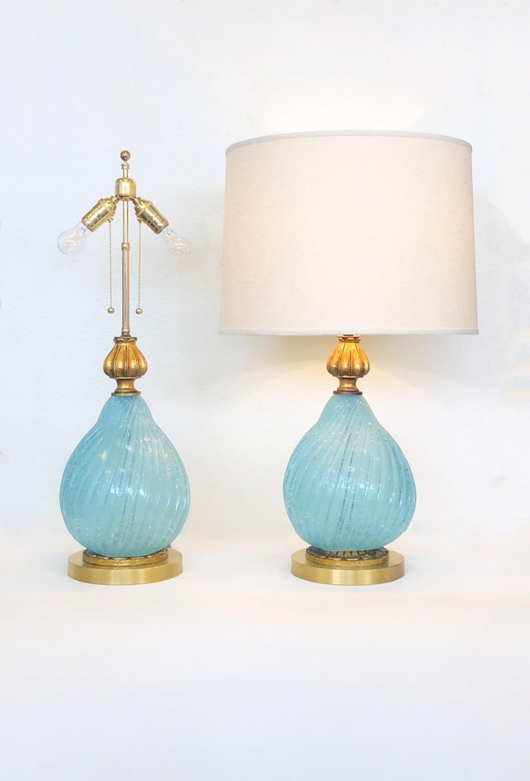 Glamorous pair of powder blue Murano glass and brass table lamps from the 1960’s.
Newly rewired with new brass hardware and new vanilla linen shades. 
Parts of the lamps are carved wood that’s gold leaf gilded.
Measurements: 18.5” diameter, 30”
