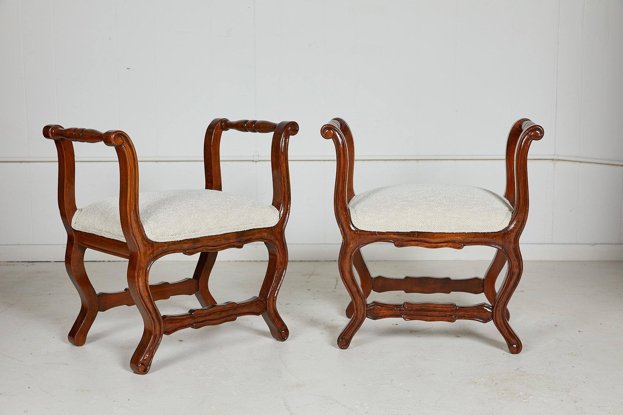 Early 20th century Italian pair of carved walnut stools in the Provencal style with upswept and turned arm rests and an upholstered seat. The seat is newly upholstered in a cream and tan tweed by Jim Thompson fabrics.
