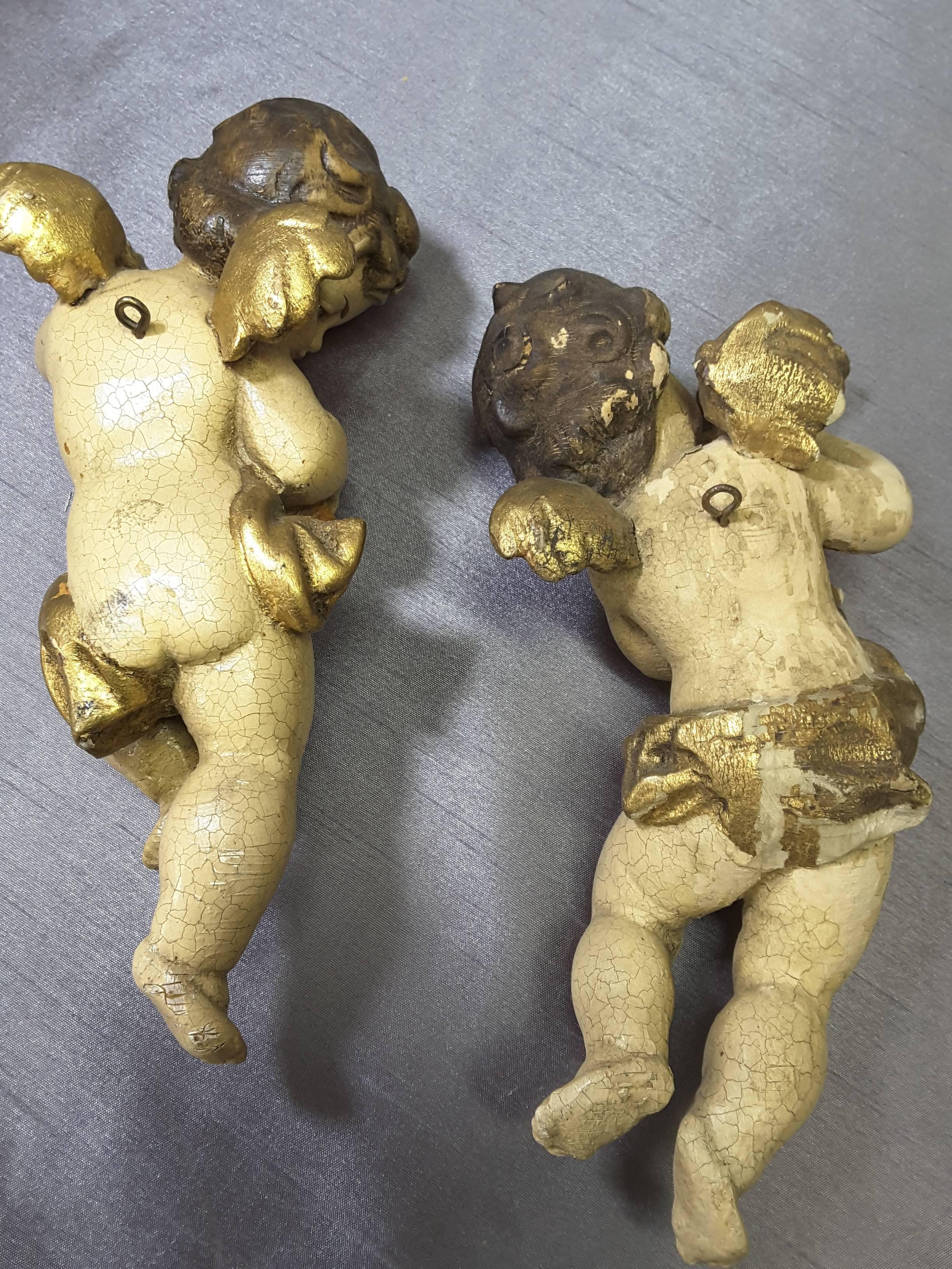Pair of Italian putti wood carved hand-painted gilt, late 19th-early 20th century, each playing an instrument, Horn & Mandolin, Gilt wings and loin cloth. The putti have back rings for hanging, minor paint loss on the back of one putti as per photo,
