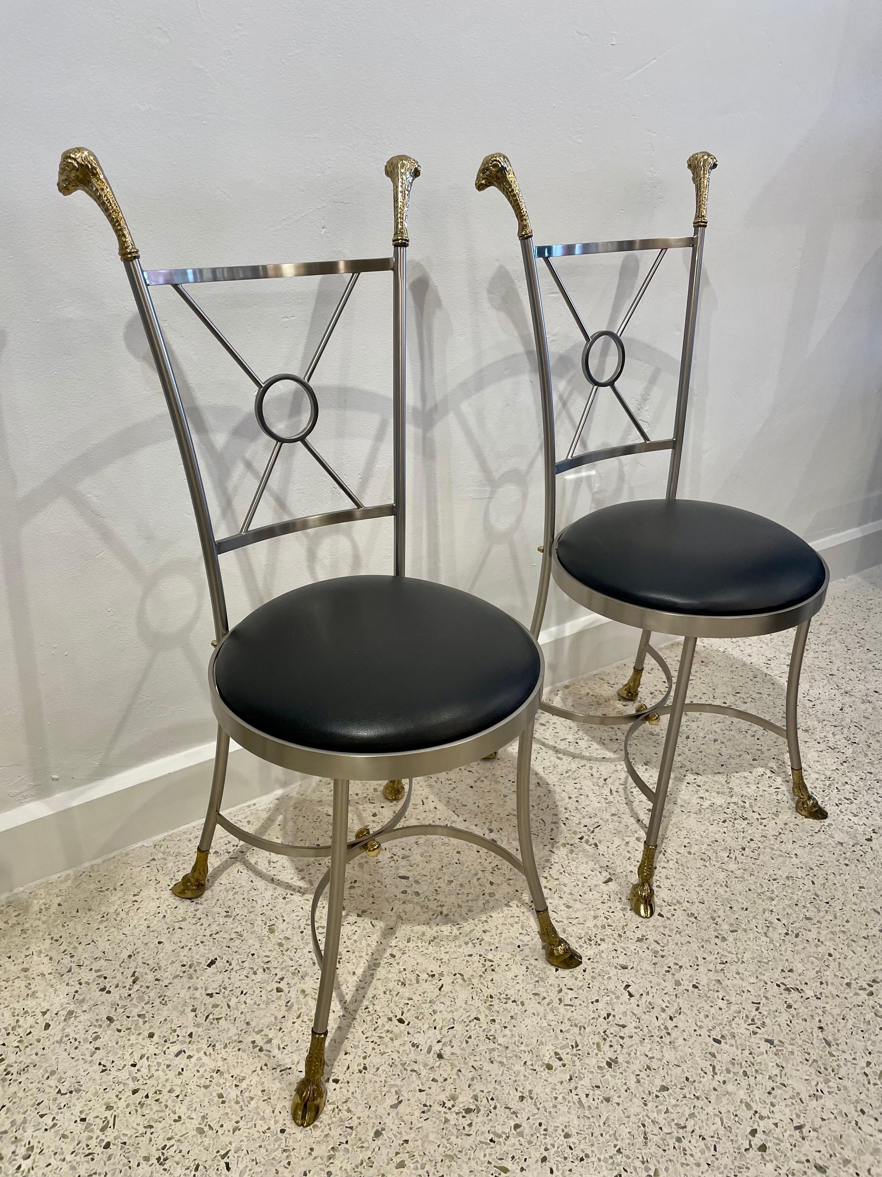 Mixed-metal (brushed steel and brass), these chairs with rams head finials and hooved feet, are newly upholstered in black leather. Made in Italy 1970's, likely by Maison Jansen, these heavy chairs are in amazing condition.
