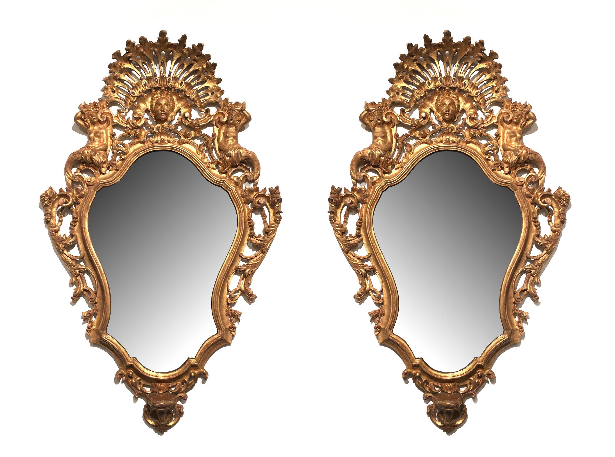 Italian Rococo (Florentine 19th century) pair of carved giltwood wall mirrors with a pierced fan shaped relief flanked by figures and a central head and all-over elaborately carved.
