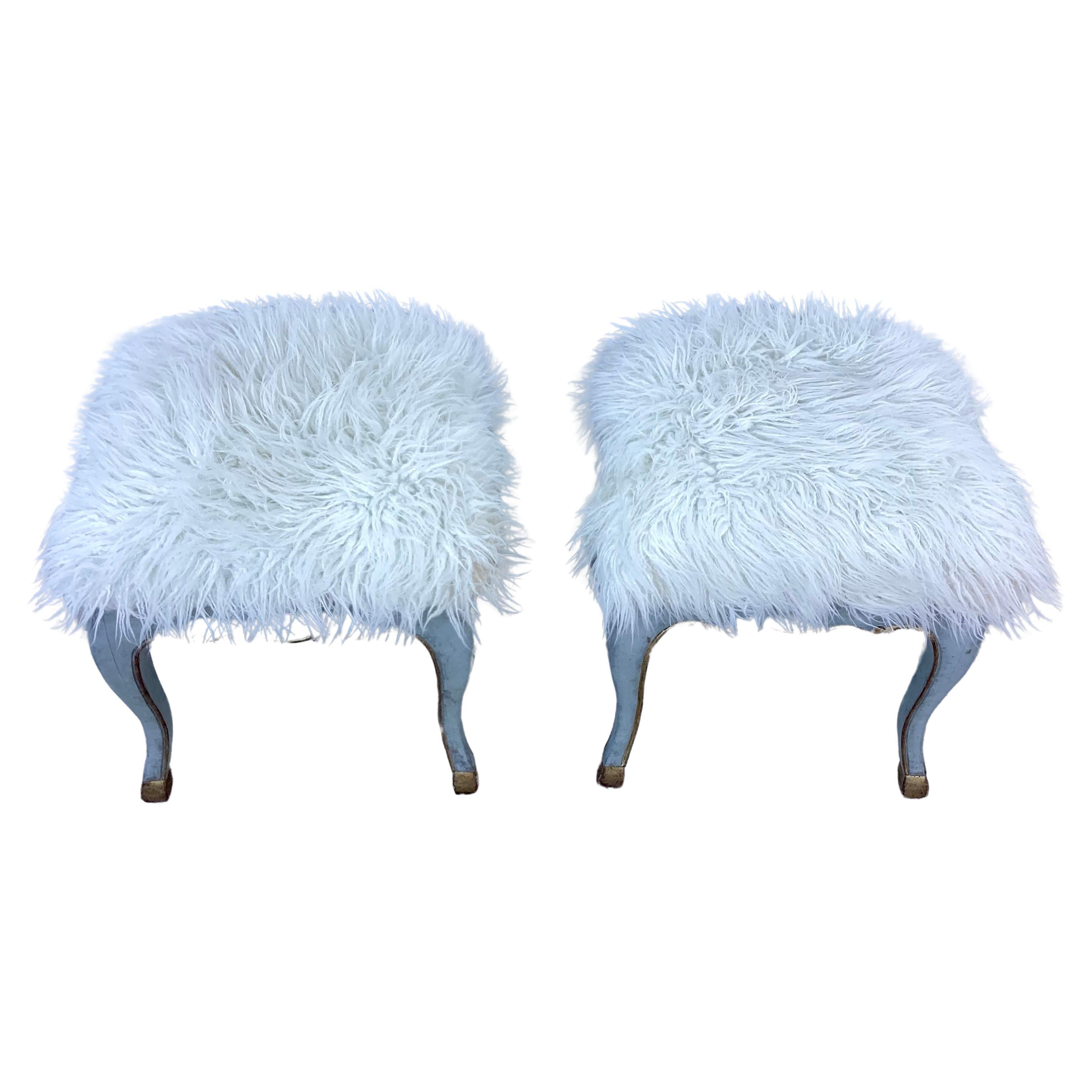 Pair of mid-century modern Italian Rococo stools with faux sheepskin seats. Base is made of wood painted in a light blue with gold trim with gilt feet on cabriole legs. Thick white faux sheepskin sits atop of each stool. Add a touch of glamour to