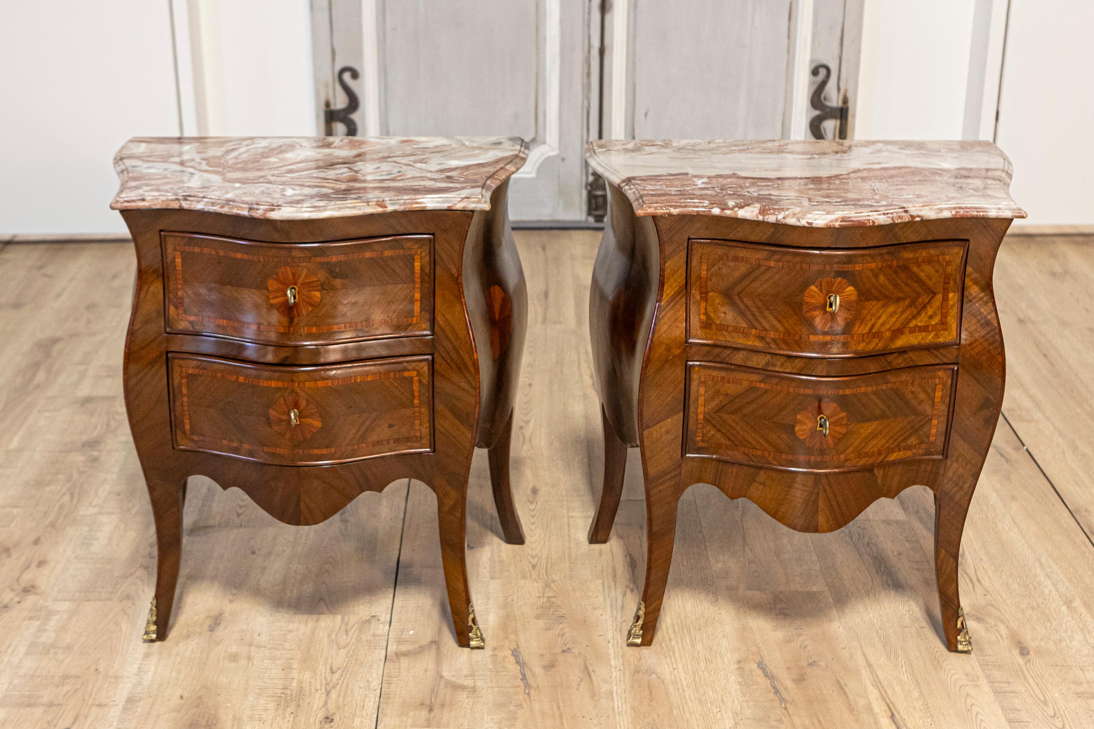 A pair of Italian Rococo style bombé walnut bedside tables from circa 1900 with marble tops and carved aprons. This elegant pair of Italian Rococo style bombé bedside tables from circa 1900 is an exemplary addition to any refined bedroom setting.