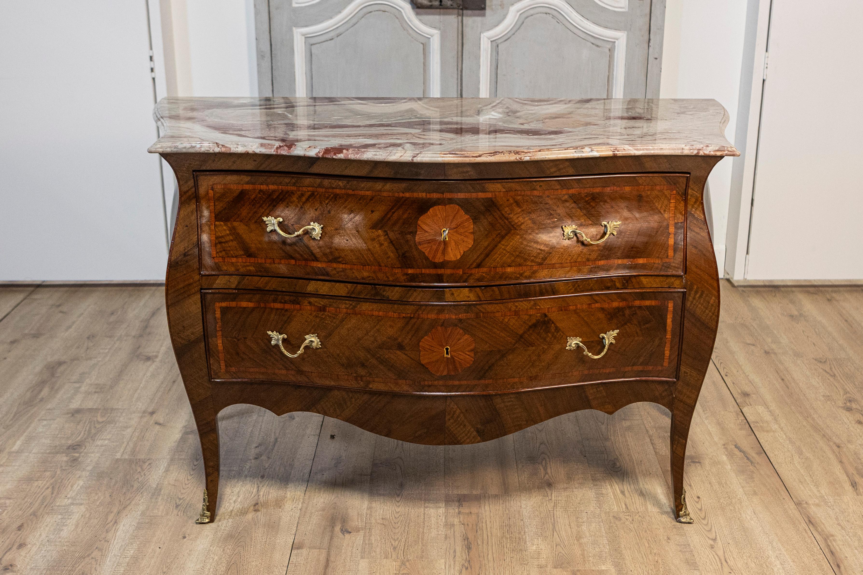 A pair of Rococo style walnut and mahogany bombé commodes from circa 1900 with marble tops and bronze hardware. This exquisite pair of Rococo style bombé commodes, crafted around 1900, elegantly combines walnut and mahogany woods with sophisticated