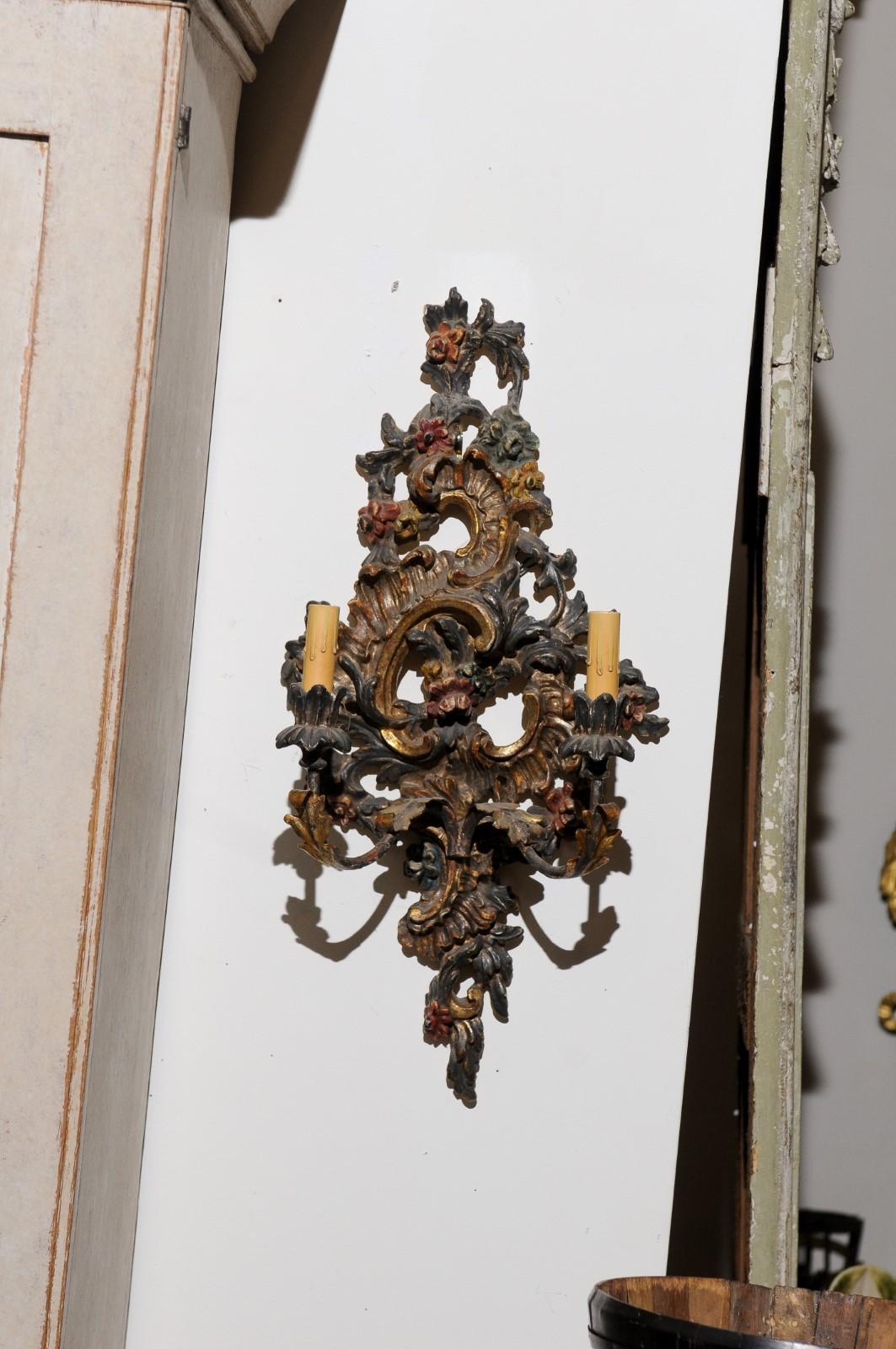 A pair of Italian Rococo style painted and carved, wood and metal two-light sconces from the late 19th century. Born in Italy during the last decade of the 19th century, each of this pair of wall sconces features a carved Rococo Silhouette,