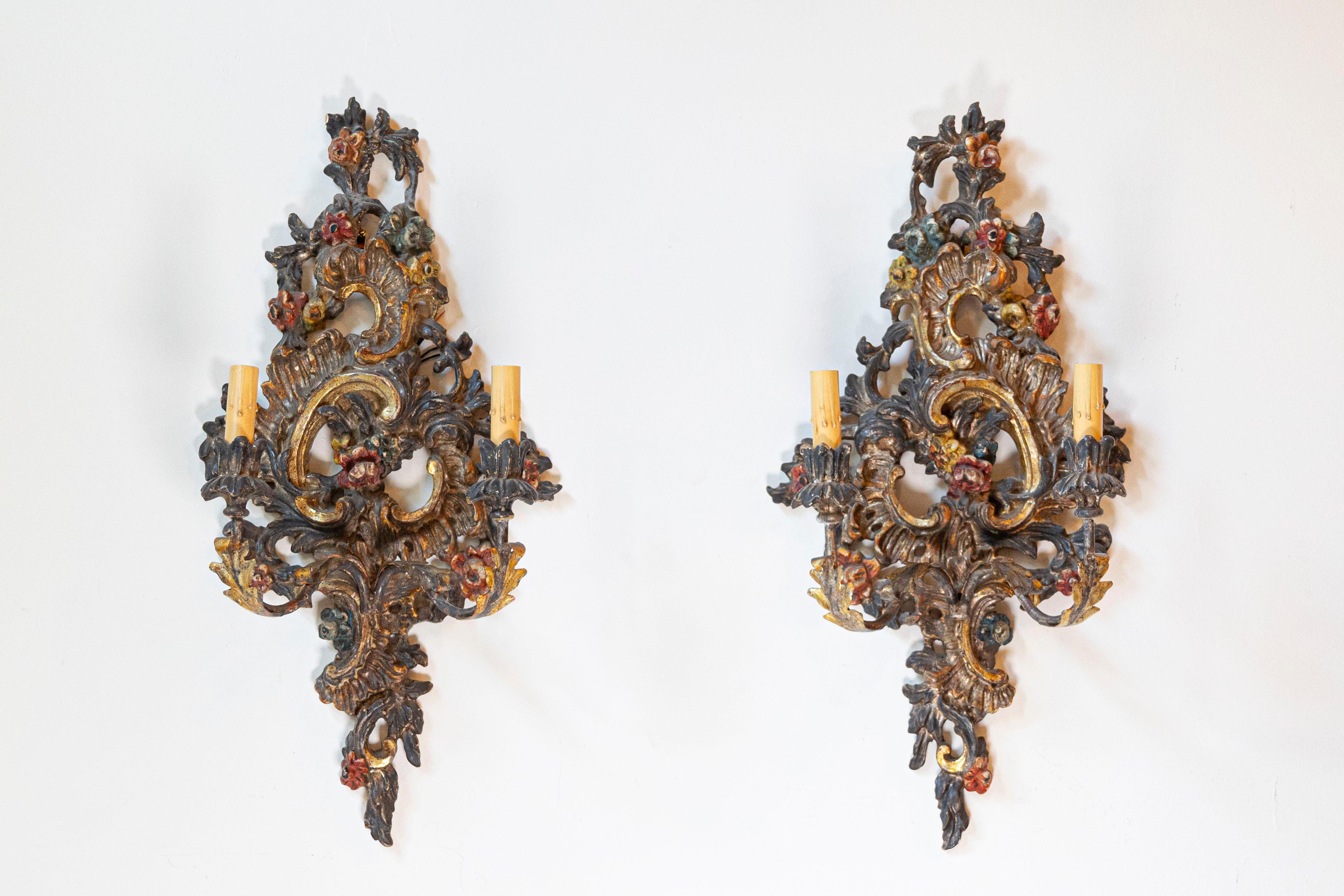 Paire d'appliques à deux lumières de style rococo italien, peintes et sculptées, en bois et en métal, de la fin du XIXe siècle. Née en Italie au cours de la dernière décennie du XIXe siècle, cette paire d'appliques murales présente une Silhouette