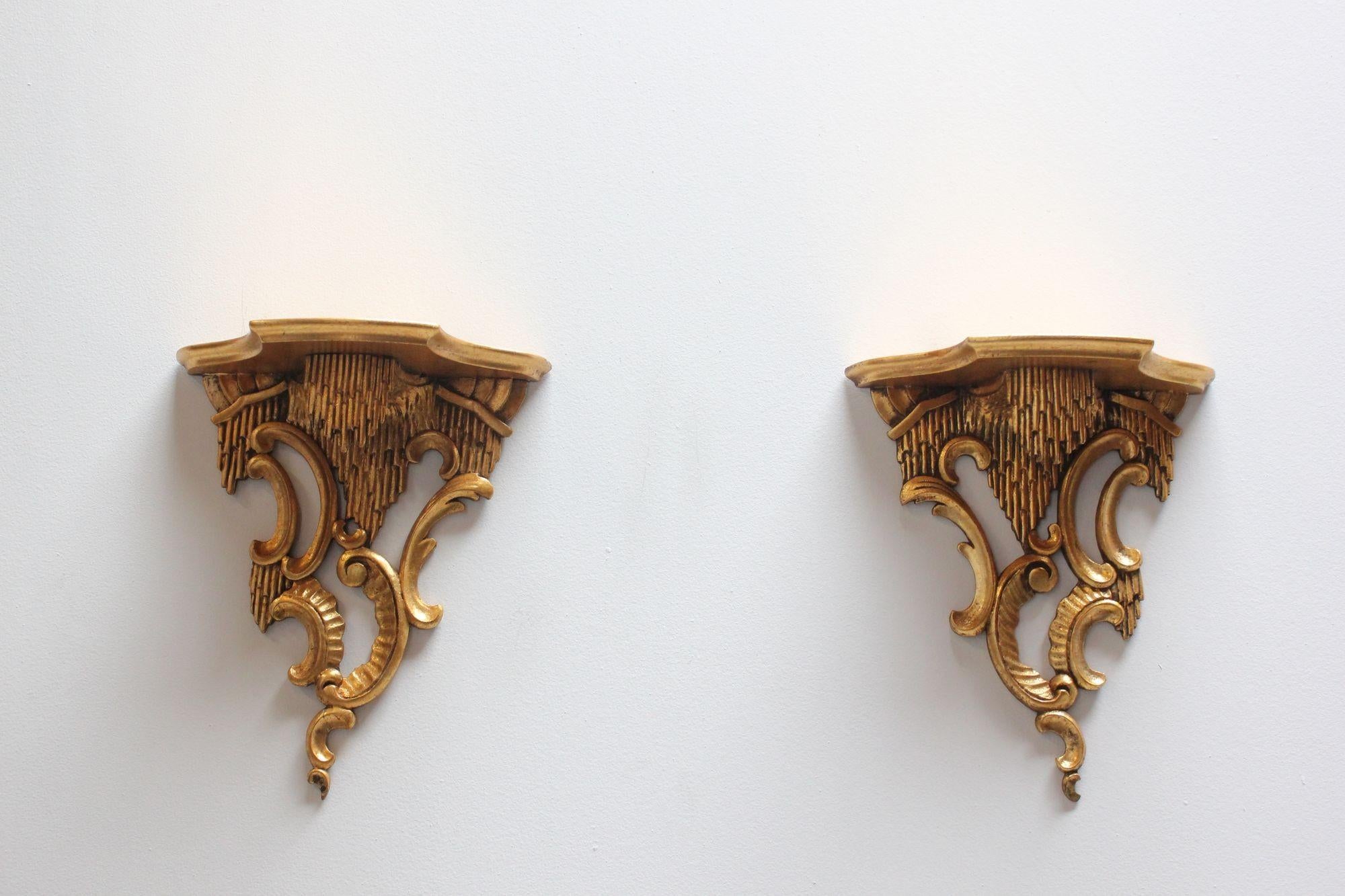 Pair of gilded Italian Rococo-style wall brackets (ca. 1950).
Deeply carved in high relief with rocaille c scroll accents and acanthus leaf decoration supporting shallow shelf surfaces. Each bracket has two hooks for hanging.
Minor gilt loss /