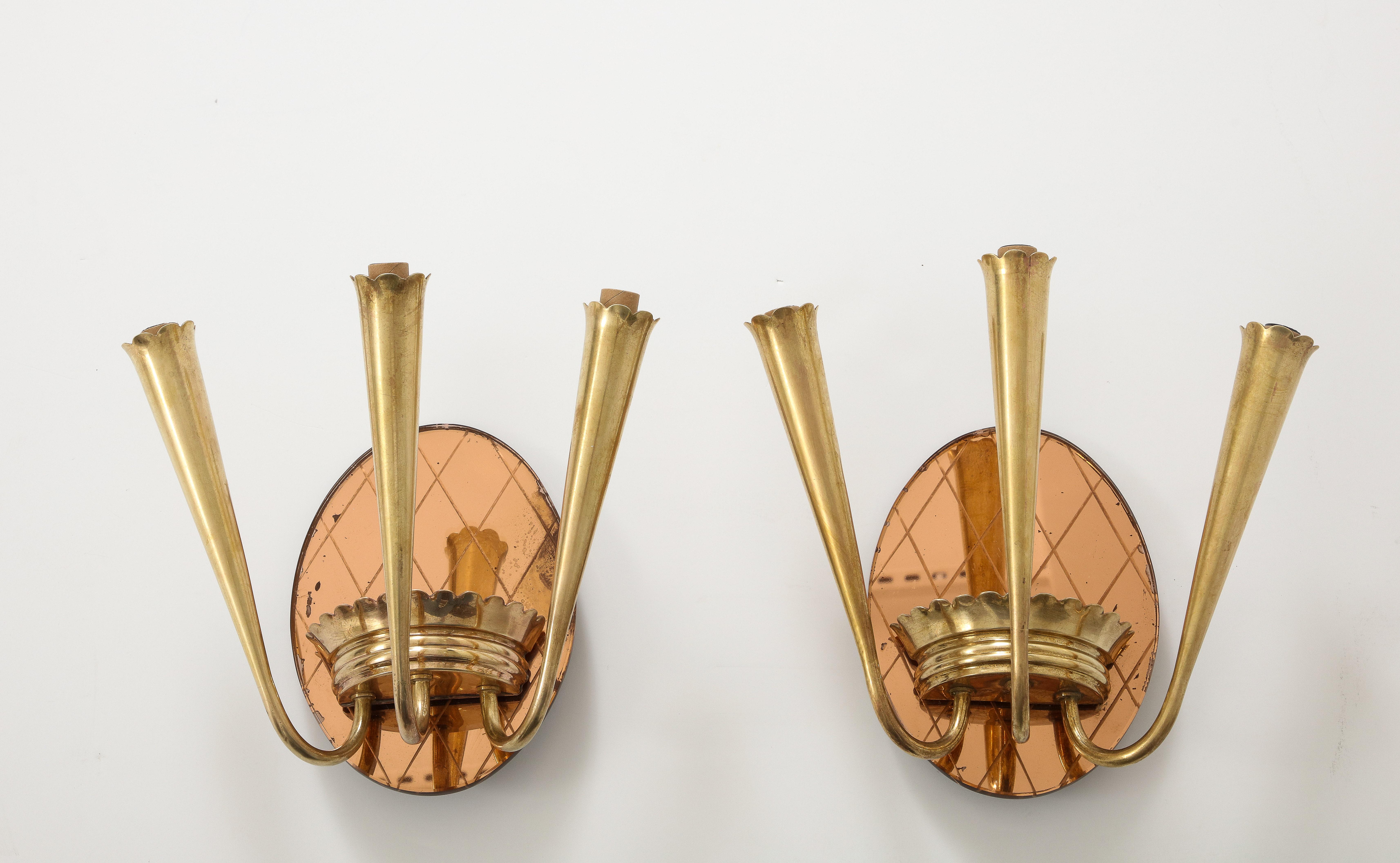Pair of Italian 1930's wall sconces, the oval back plate in rose gold glass with cross-hatched design etched into the glass.  The plate supports a stylized brass structure with banded and scalloped motif from which three brass arms radiate upward