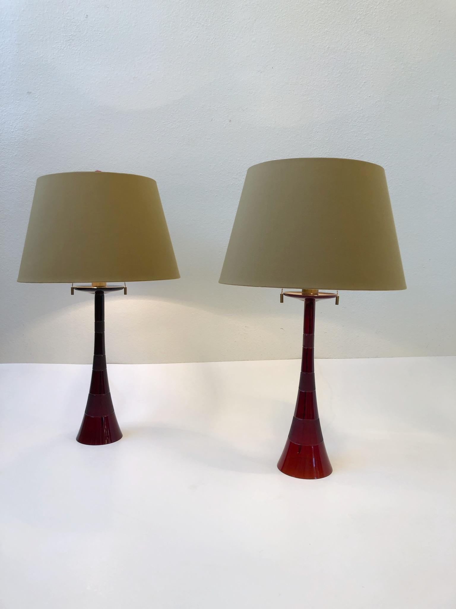 A glamorous pair of Italian ruby red Murano glass table lamps in the shape of a trumpet with satin brass hardware and original shades. The lamps were designed in the 1980s by John Hutton for Donghia. Both lamps are signed Donghia. One of the lamps