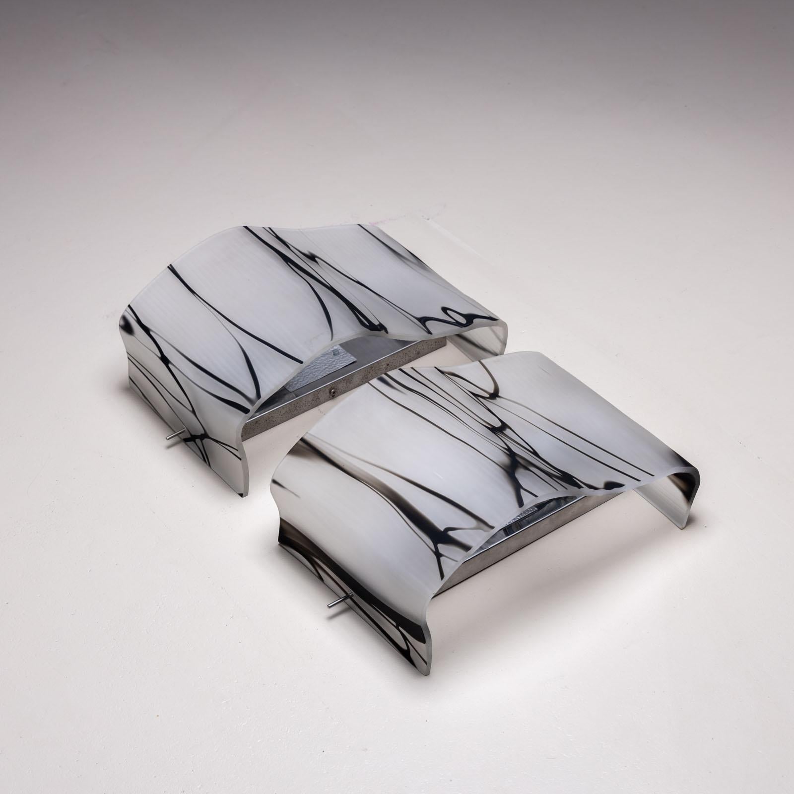 Pareja de apliques de pared con pantallas onduladas de cristal ahumado blanco con sutiles inclusiones negras. Las pantallas están montadas en soportes de pared niquelados con zócalo. 