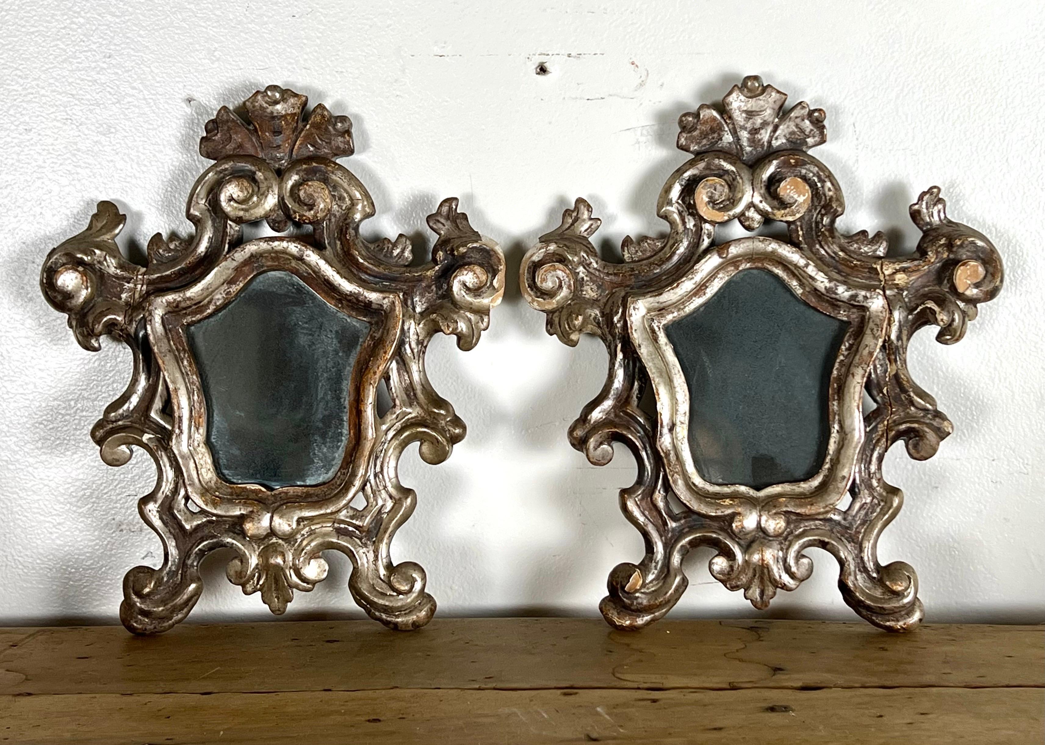 A pair of petite scroll shaped 19th-century Italian silver-leaf, Baroque-style mirrors.  The combination of the intricate Baroque-style design with the scroll shapes adds character and elegance to the mirrors.  They would make great decorative