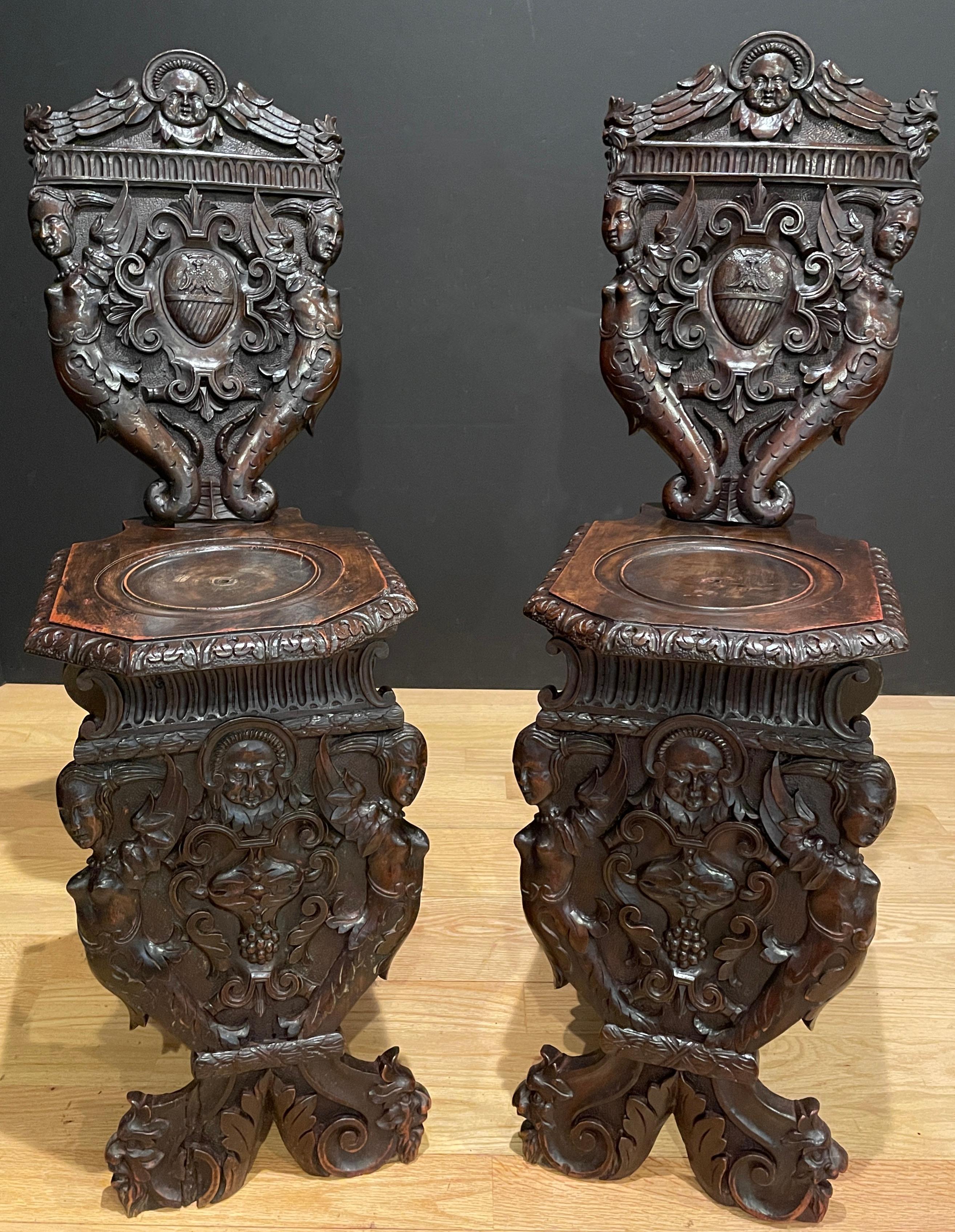 Antikes Paar figuraler, stark geschnitzter Nussbaum-Sgabello-Stühle. 
Geflügelte Figuren und barocke Muster.
Der sgabello ist eine Art Stuhl oder Hocker mit geschnitzten und oft kunstvoll verzierten Holzbeinen und Rückenlehnen. Die Form stammt aus