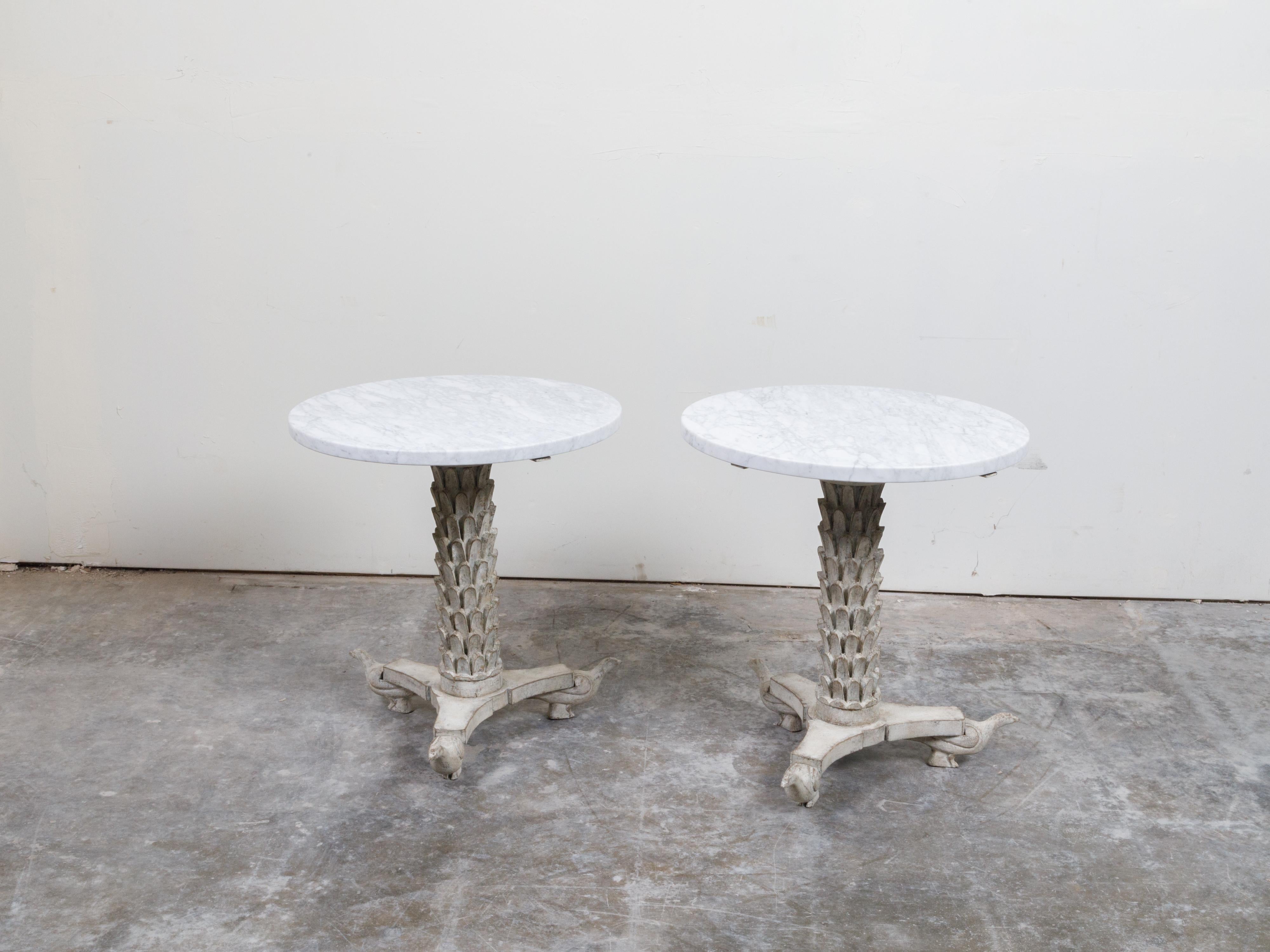 A pair of Italian carved wooden side tables from the mid 20th century, with round white marble tops, carved palm tree bases and birds. Created in Italy during the midcentury period, each of this pair of side tables features a white marble top