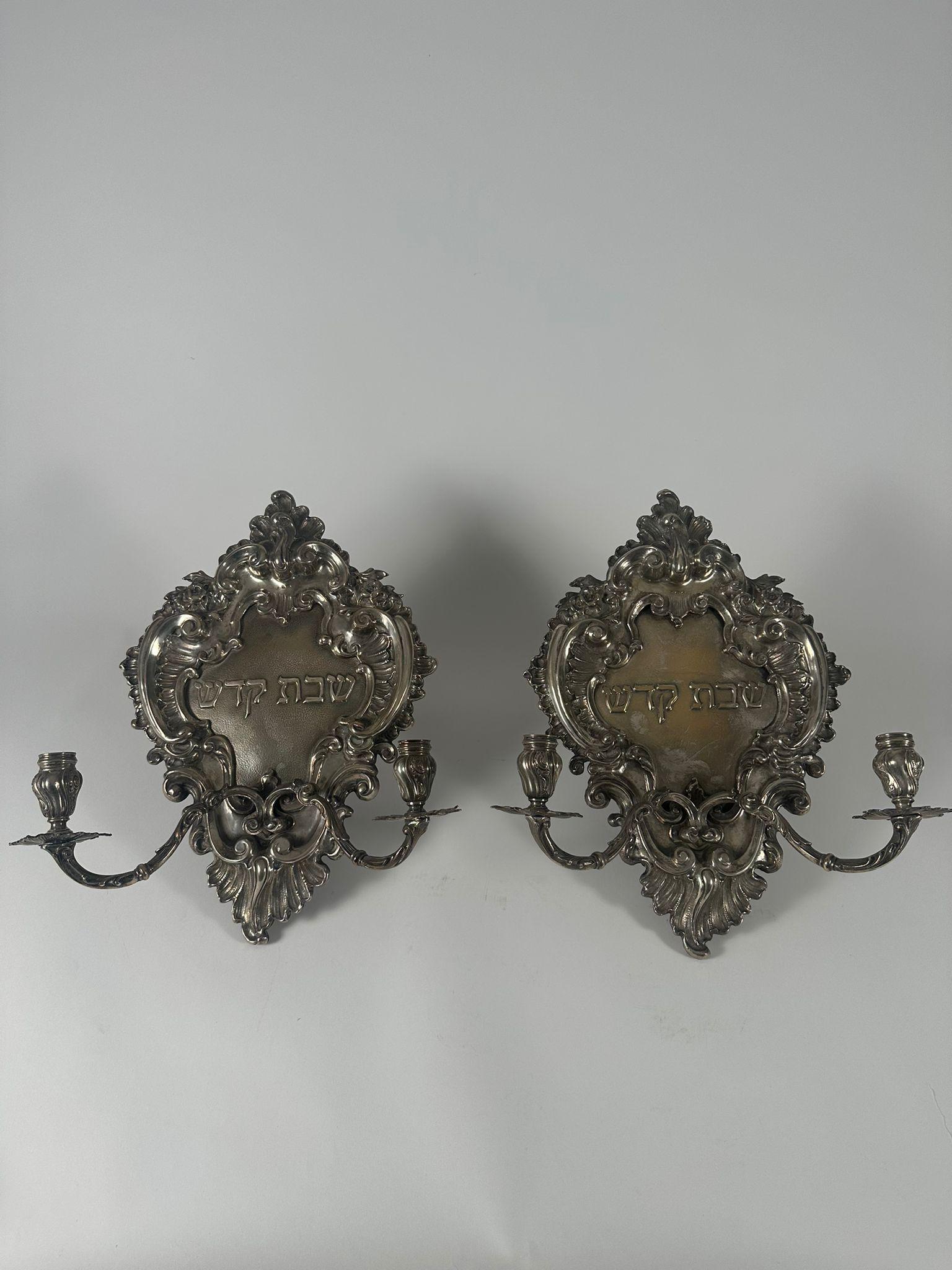 Cette étonnante paire d'appliques à bougies de Chabbat juives anciennes est fabriquée en argent 800 et porte des poinçons italiens, ce qui laisse supposer une orfèvrerie européenne experte. Chaque applique présente un opulent design de style Rococo,