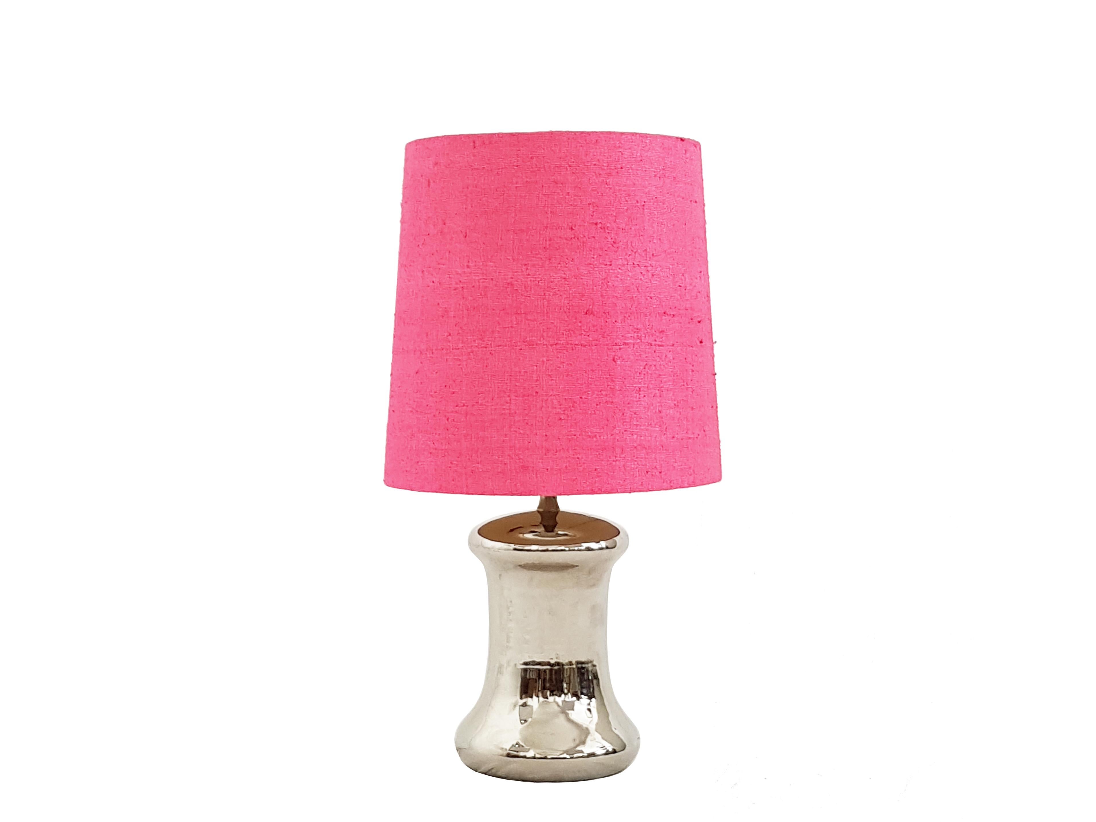 This pair of glam table lamps was produced in Italy around the 1970s. They are made from a silvered and glazed ceramic base, with a 3-lights adjustable electrical system. They are equipped with their original pink fabric shades, which remain in fair