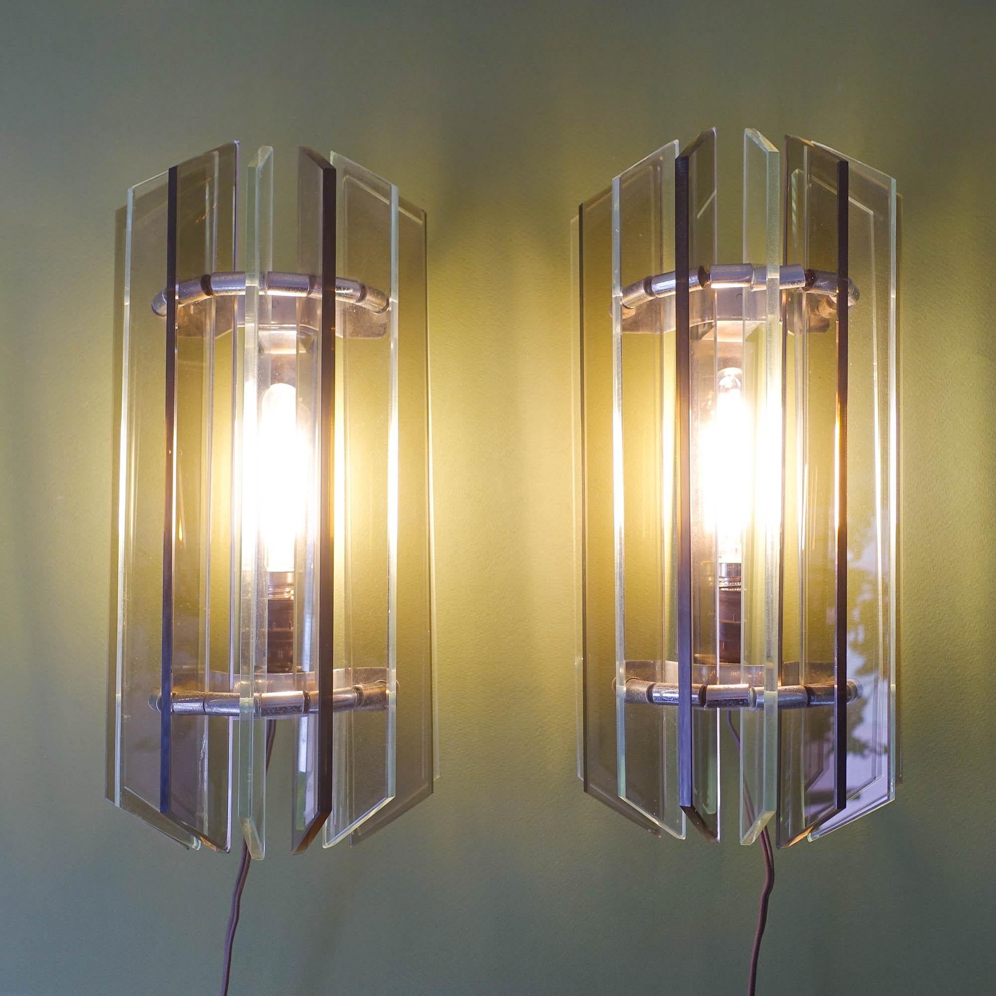 Dieses Paar Wandleuchter wurde in den 1970er Jahren in Italien im Stil von Veca entworfen und hergestellt. Jede Leuchte besteht aus 9 Glasscheiben aus klarem und geräuchertem Glas, die an einem kleinen verchromten Metallrahmen befestigt sind. In