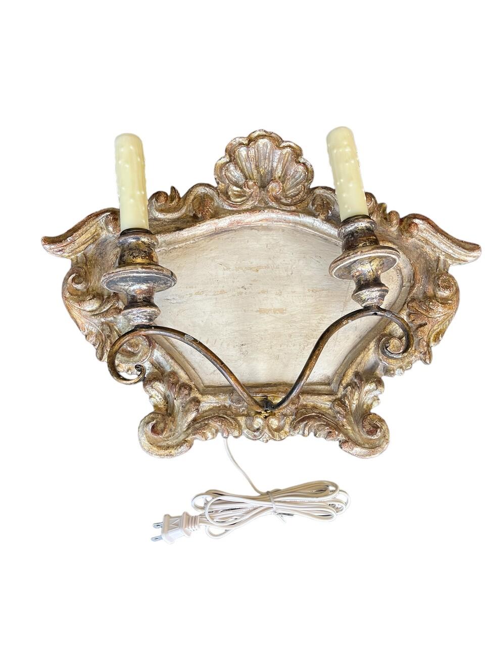 Paire d'appliques murales à 2 lumières de style italien. Bois sculpté et doré qui présente une belle finition vieillie. L'installation électrique a été refaite à neuf et est prête à l'emploi. Peut également être encastré.