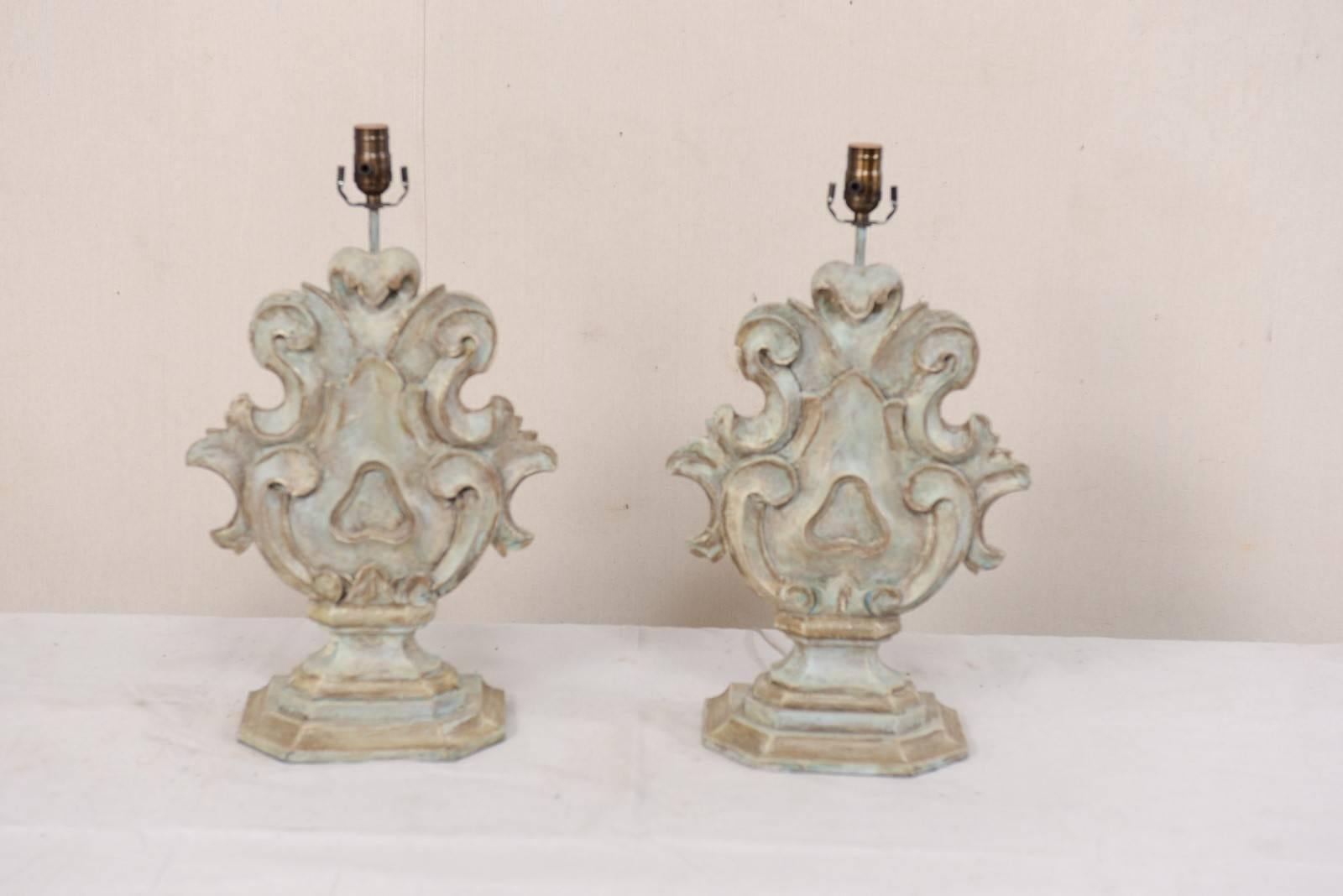 A pair of Italian style painted and carved and painted wood table lamps. This pair of table lamps feature curvy scroll and acanthus leaf motif carved bodies, raised up on a stepped up, half octagonal base. The primary color of this pair is a wash of