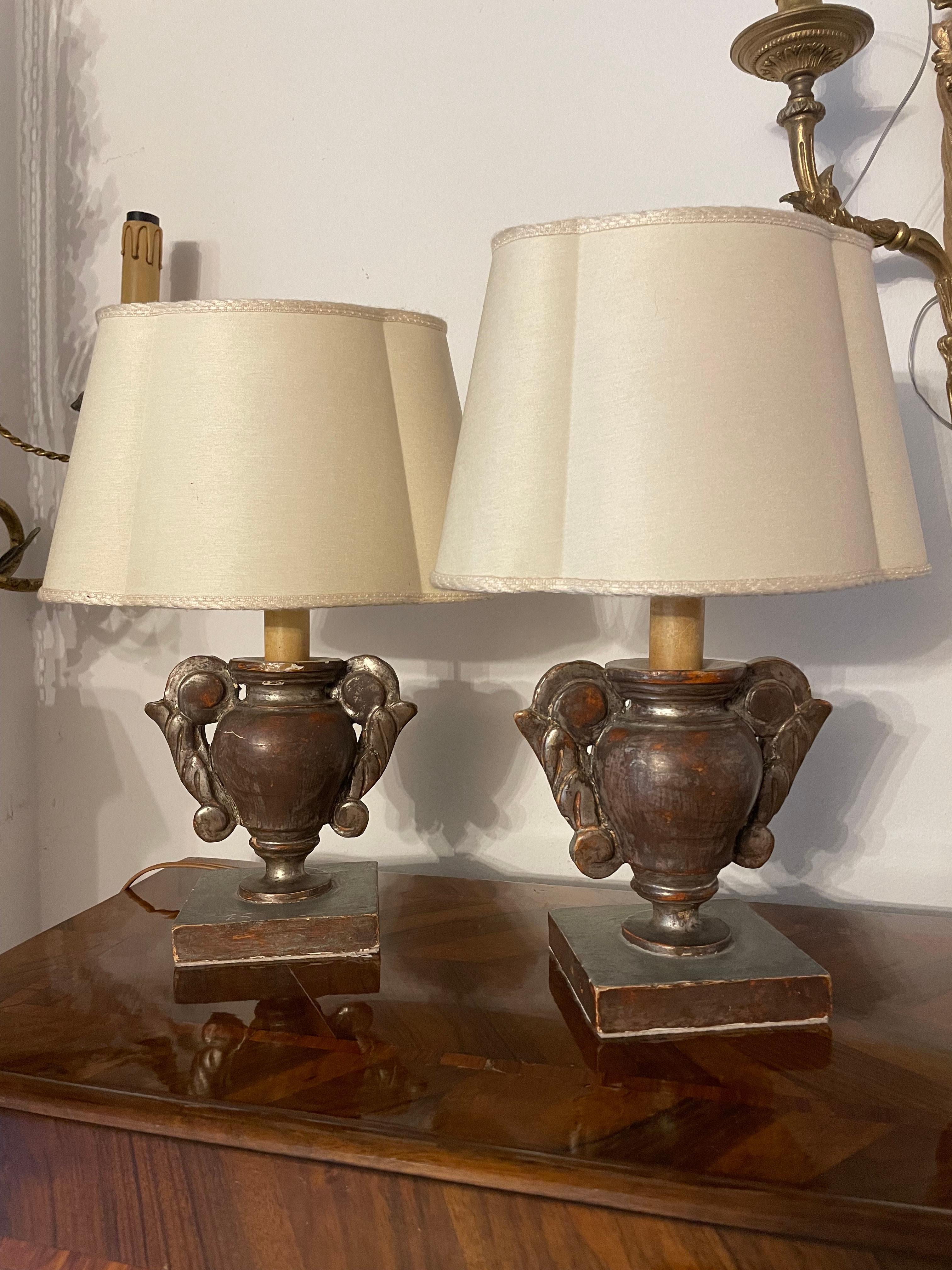 A pair of early 19th century Italian silver-leaf wooden small bedside table lamps, consisting of two antique portapalme vases, on square base, turned Cembran pinewood with shaped scrolling handles.
Mounted as small lamps with new oval-shaped