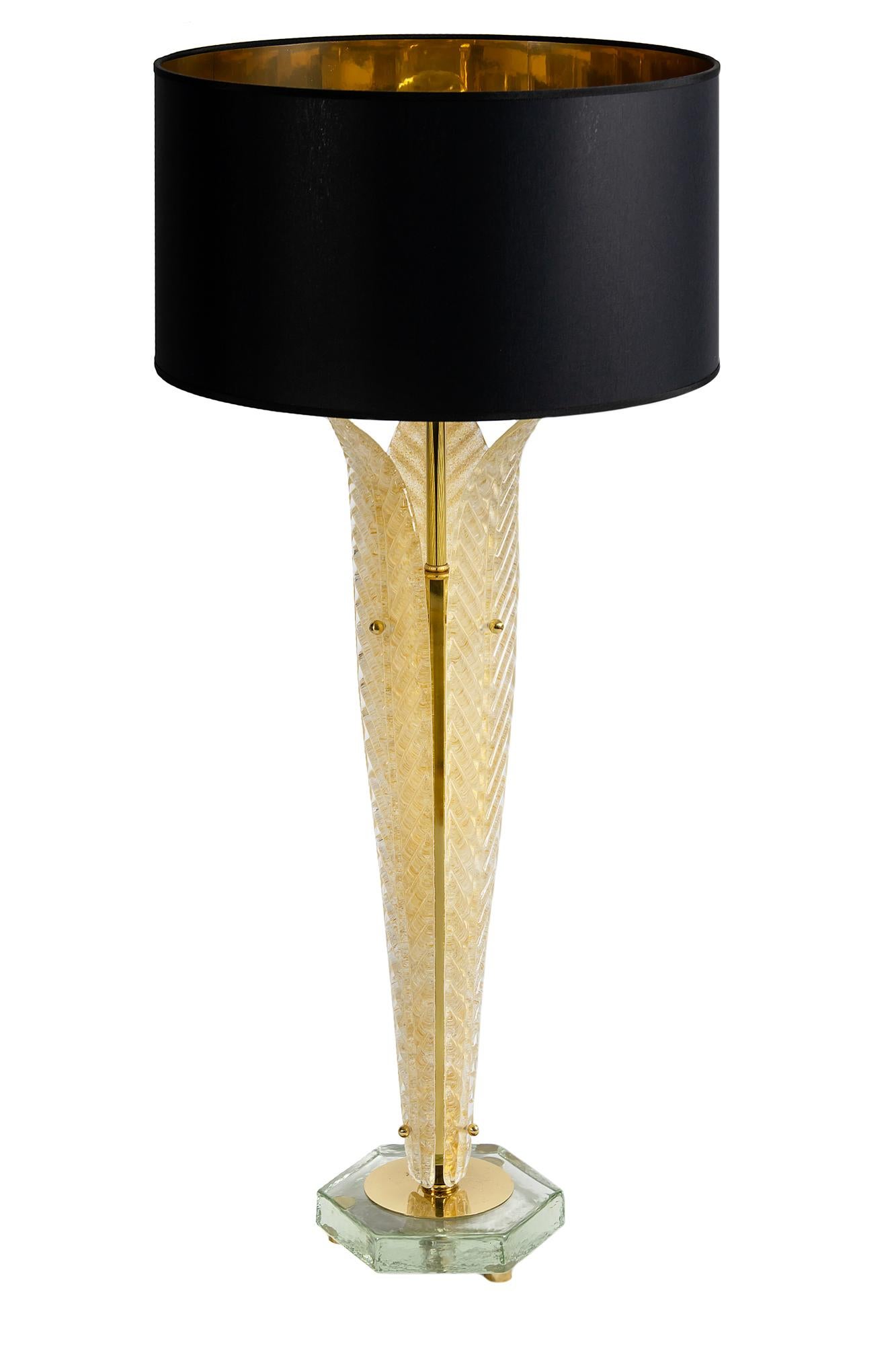 This pair of Italian table lamps are made of 3 pieces leaf form Murano glass. The glass is lightly golden. The base is made of polygon form thick clear glass with small round brass legs. Both lamps are with new made satin finish black color textile