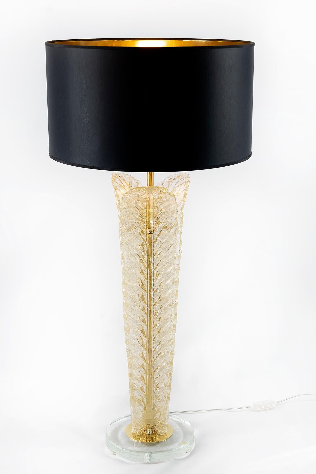 This pair of Italian table lamps are made of 3 pieces leaf form Murano glass. The glass is lightly golden. The base is made of round form thick clear glass with small round brass legs. Both lamps are with new made satin finish black color textile