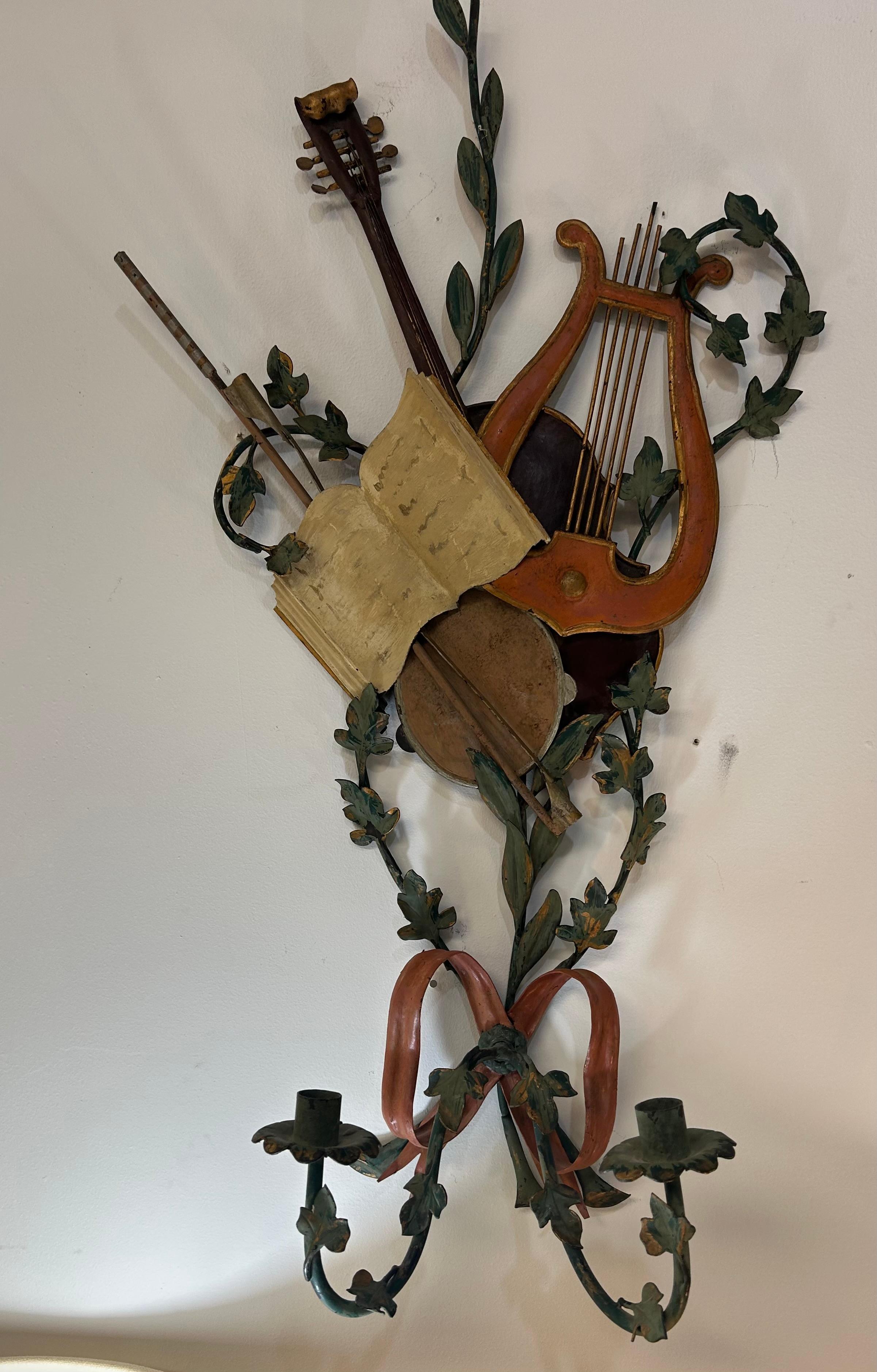 A large three dimensional pair of tole sconces with a musical motif . The paint is all original. The condition is very good… each has two candleholders with acanthus leaves.. The metal is very high-quality and is a nice combination of structures