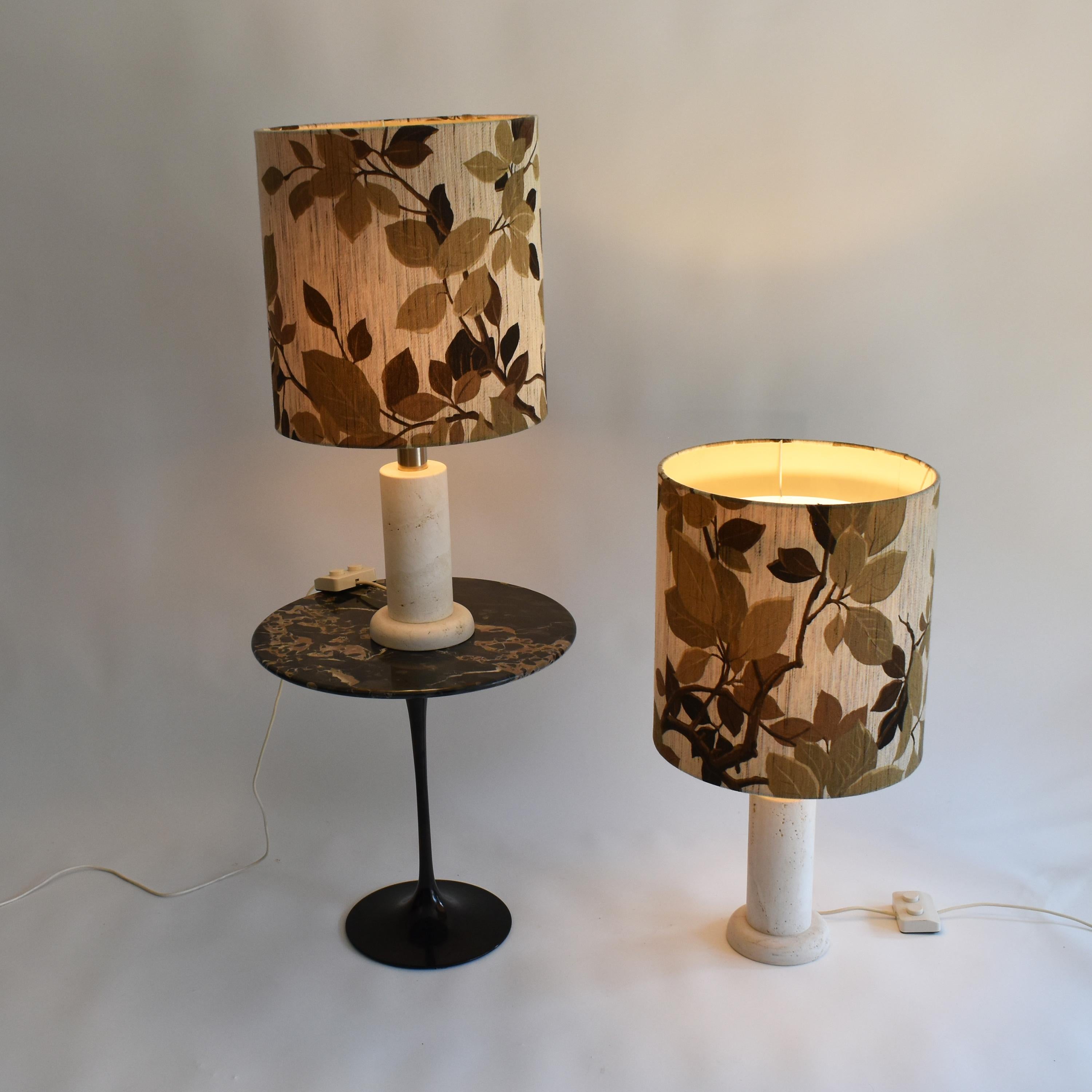 Set of two italian travertine table lamps, made in the seventies.
Excellent condition. There is one bulb facing up, to illuminate the ceiling, and create ambiance, and two bulbs behind the shade. 
The special switch allows to light the upper, the