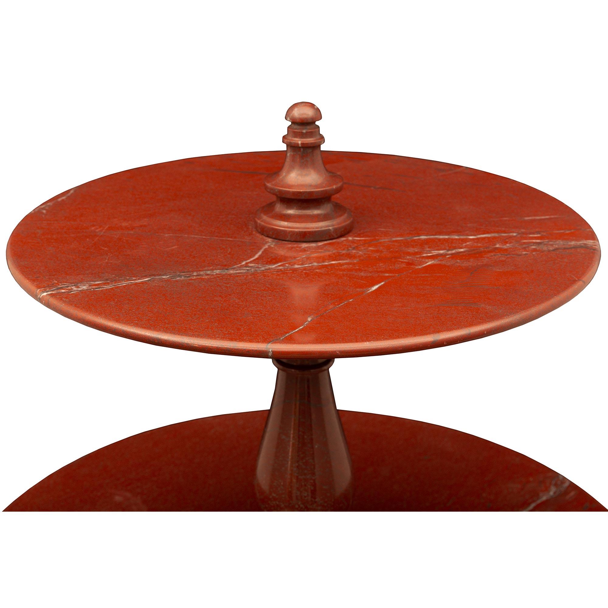 A stunning and rare pair of Italian turn-of-the- century rouge antique de Grece marble three-tier tables. Each striking table is raised by a circular mottled base with three bun feet. Leading up the baluster-shaped supports are three elegant tiers