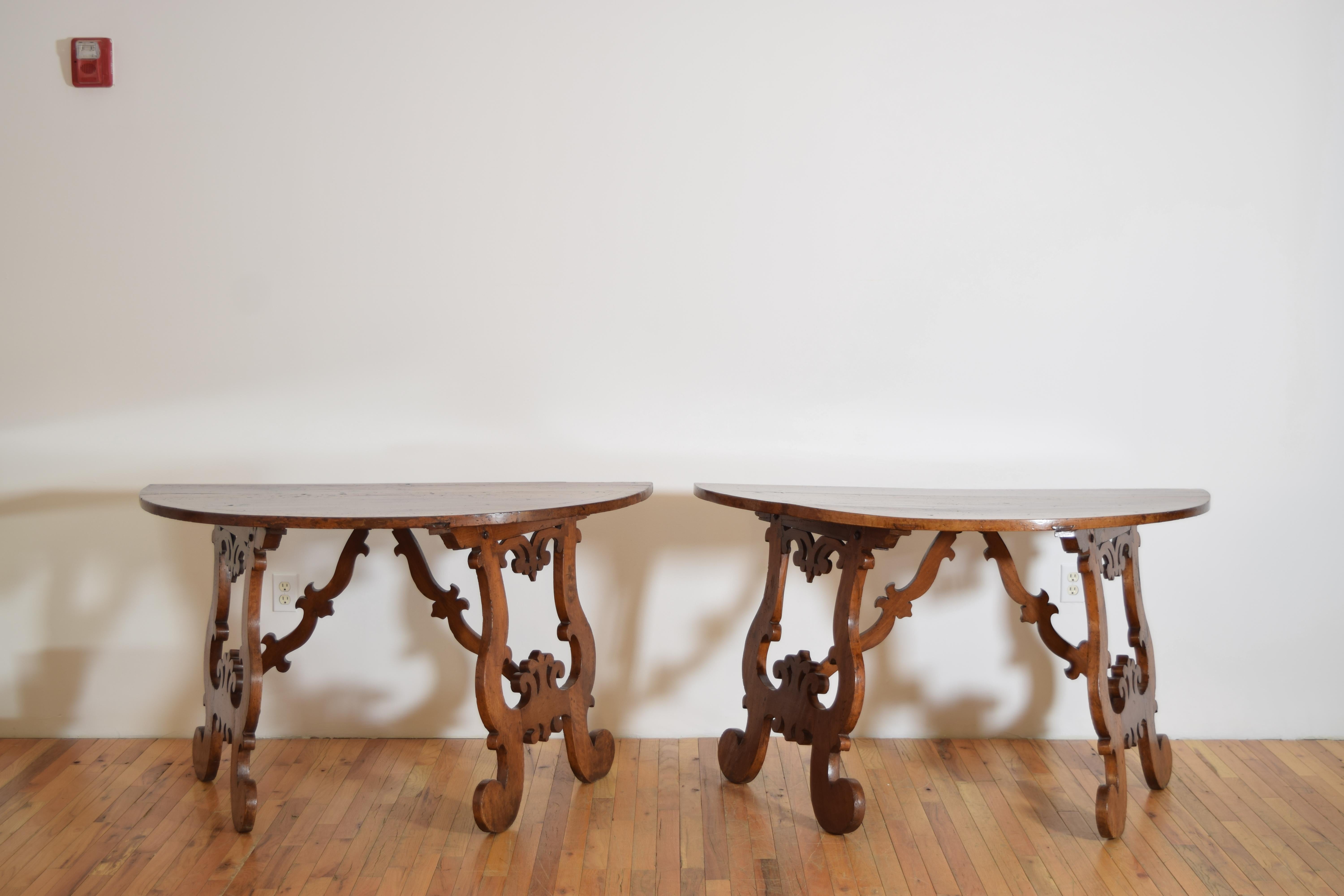 each console having a demilune shaped top with fruitwood line inlay, the tops resting on shaped double trestle-form supports, the trestles with shaped stretchers attaching to the top, curled feet