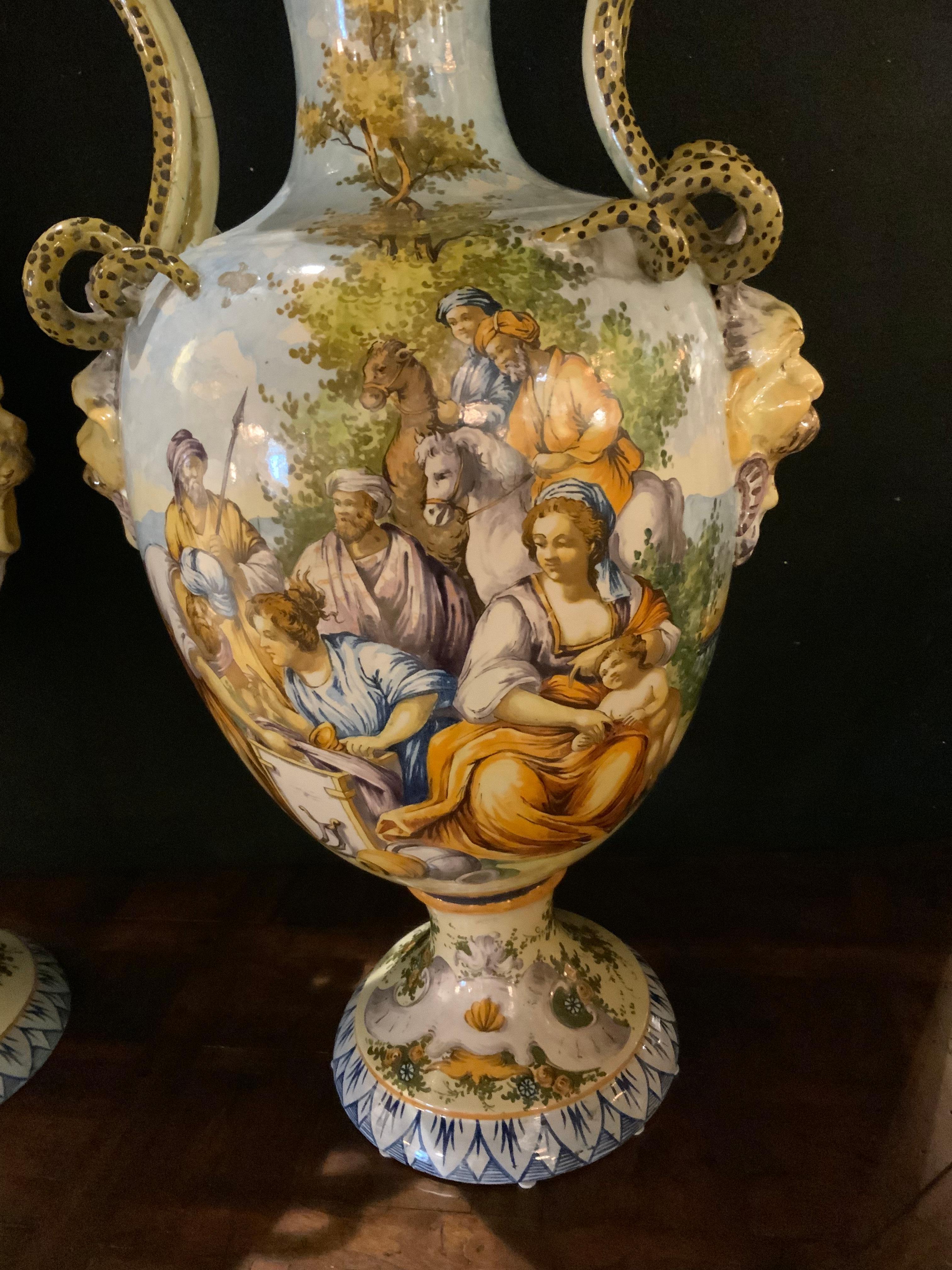 This pair of majolicas vases are very colorful and decorative 
Pieces. Well painted with old world scenes and characters 
In full dress indicative of the time. Large handles in the form
Of serpents decorate the sides of these colorful