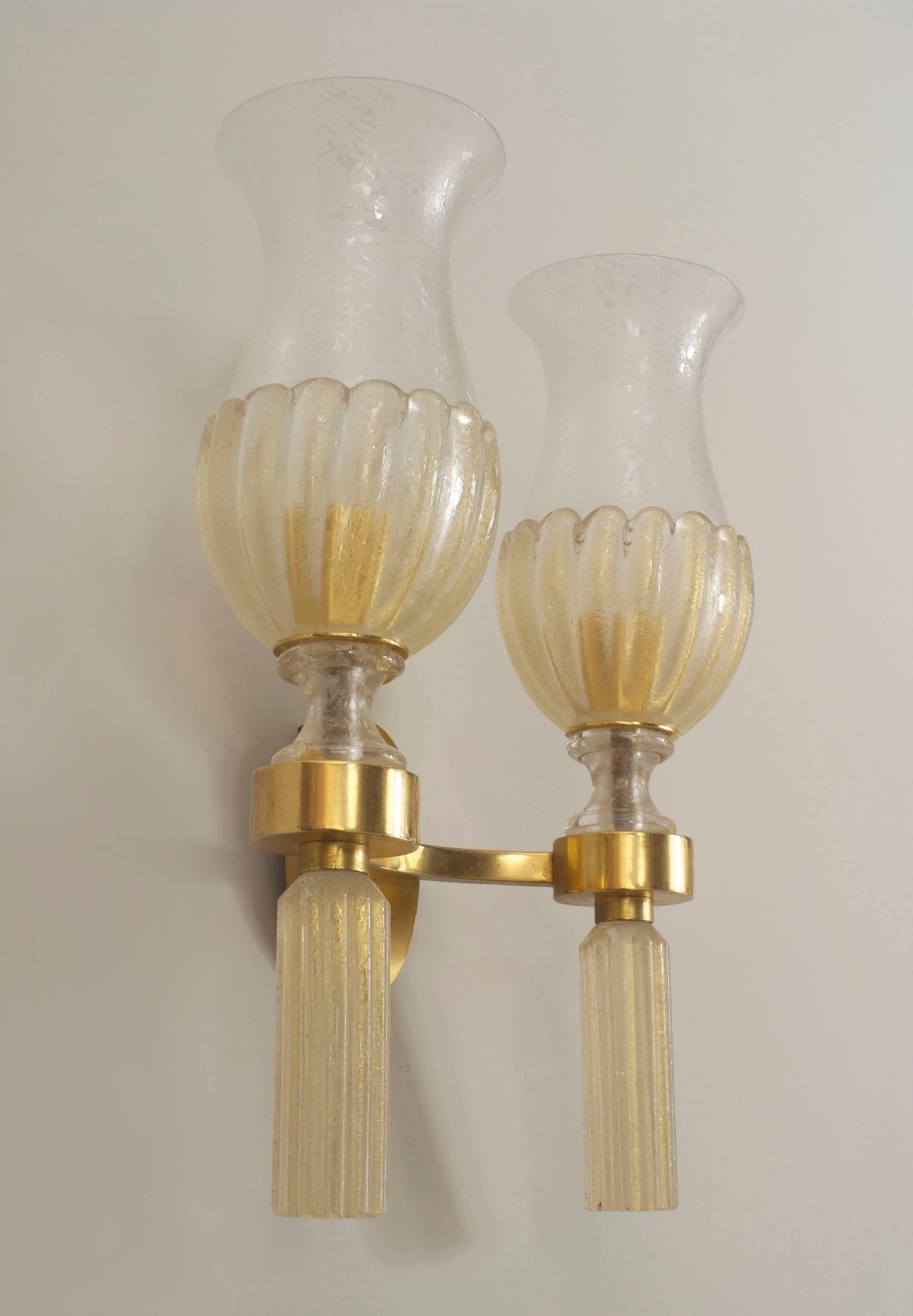 Pair of Italian Mid-Century (1940s) Venetian Murano gold dusted glass wall sconces supported by a gilt bronze two-arm frame holding shades with a fluted bottom above cylindrical fluted finals. (PRICED AS Pair)
