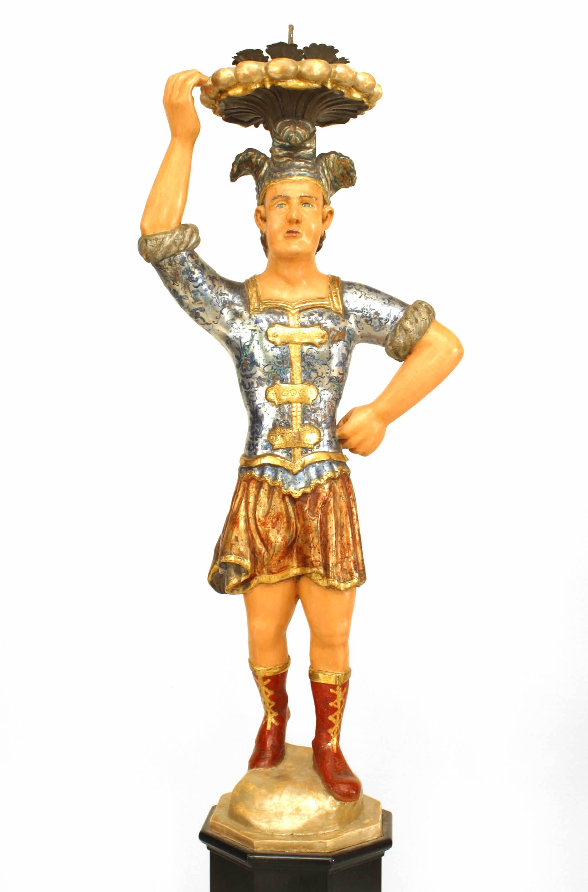 Paire de figurines italiennes vénitiennes peintes avec des chemises bleues et des shorts rouges polychromés et une coiffe à plumes ; support de bougie et support sur une base ébénisée à 8 côtés.
