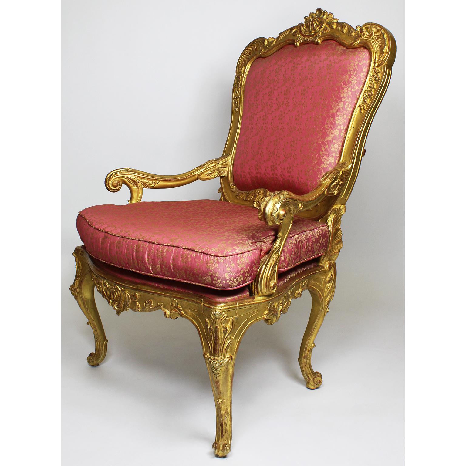Paire de fauteuils trône en bois doré de style rococo vénitien italien. Les cadres ornementalement sculptés avec de larges accoudoirs ouverts et enroulés, un dossier rembourré couronné d'un cimier en coquille sculpté en bois doré et de motifs