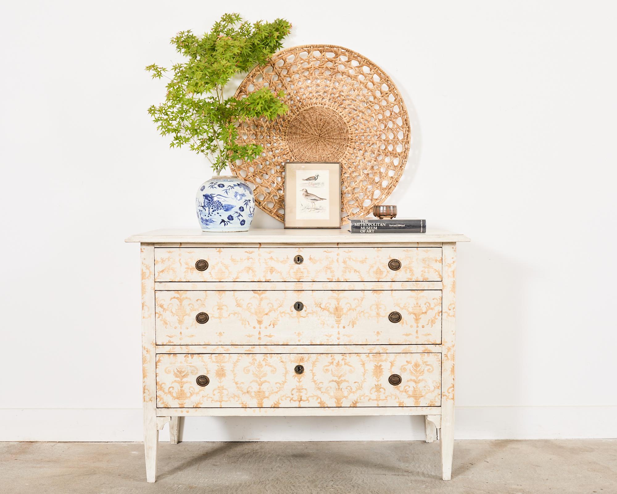 Grand pair of Italian commodes or chest of drawers featuring a Venetian style painted finish. The large pine cases measure over 4 feet wide fronted by three storage drawers with patinated bronze ring pulls. The pine has an off-white ground decorated